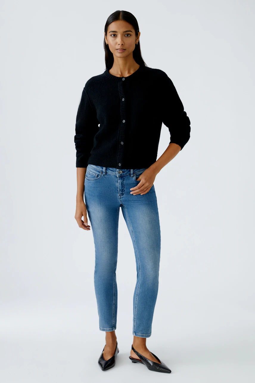 Schwarze Strickjacke: Frau in lässiger Strickjacke mit Knöpfen und Jeans steht entspannt.