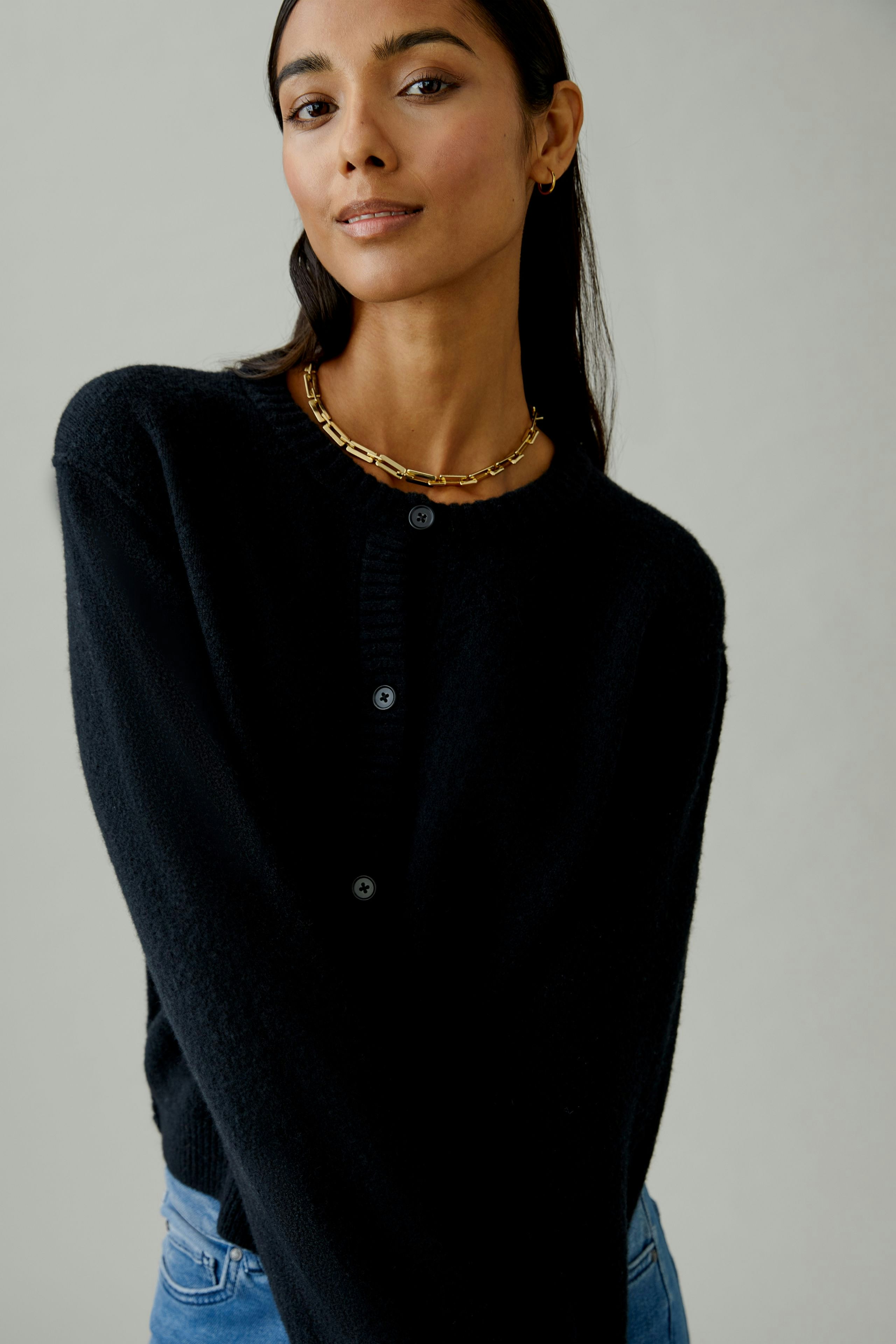 Casual women's cardigan: A woman in a black cardigan with buttons, styled with a simple necklace.