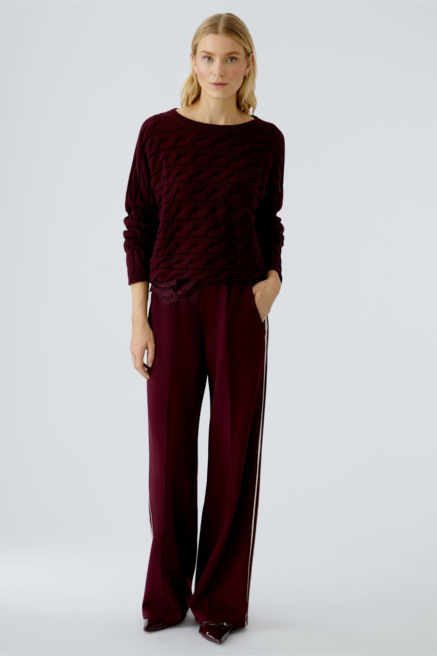 Damen-Pullover in dunklem Rot mit strukturiertem Muster, kombiniert mit lässigen, weiten Hosen.