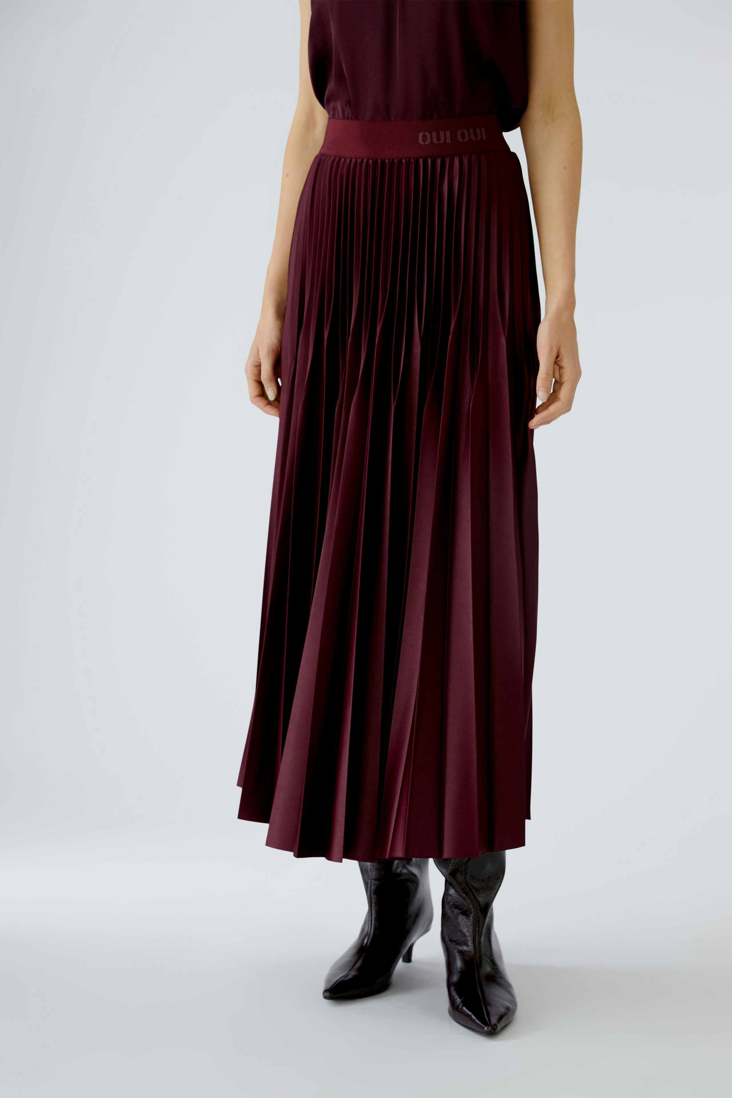 Pleated skirt: Woman wearing a burgundy pleated skirt with a comfortable waistband and stylish boots.