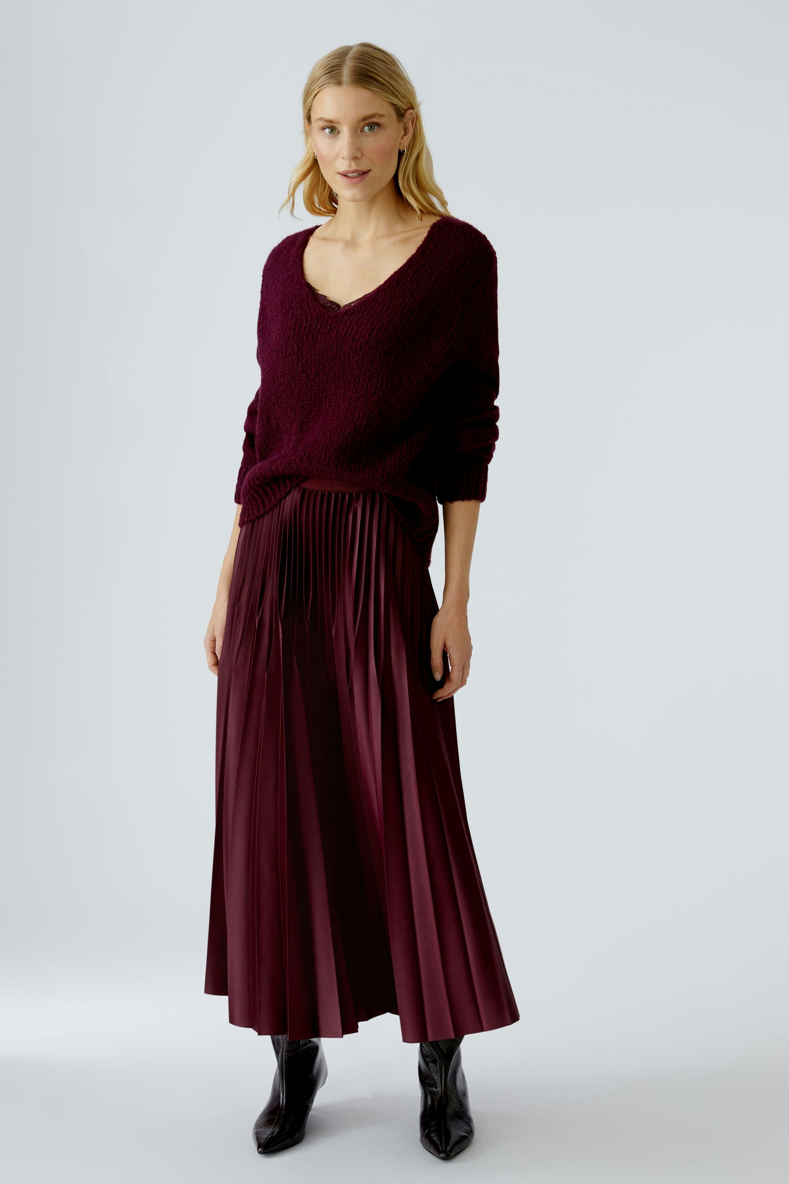 Stylish pleated skirt: Woman in a burgundy pleated skirt paired with a cozy pullover.