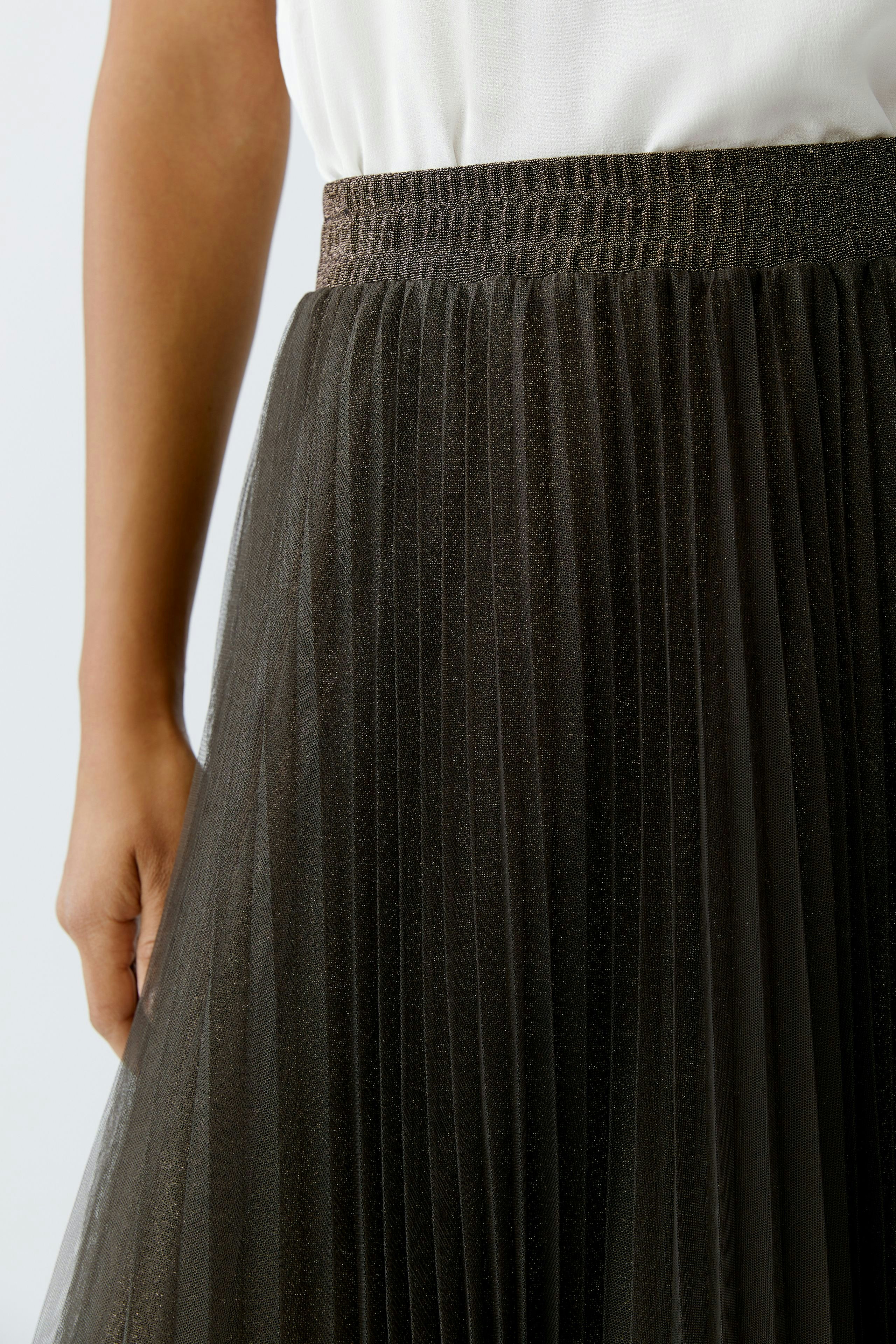 Pleated skirt: Woman wearing a black pleated skirt with a shimmering finish, paired with a simple top.