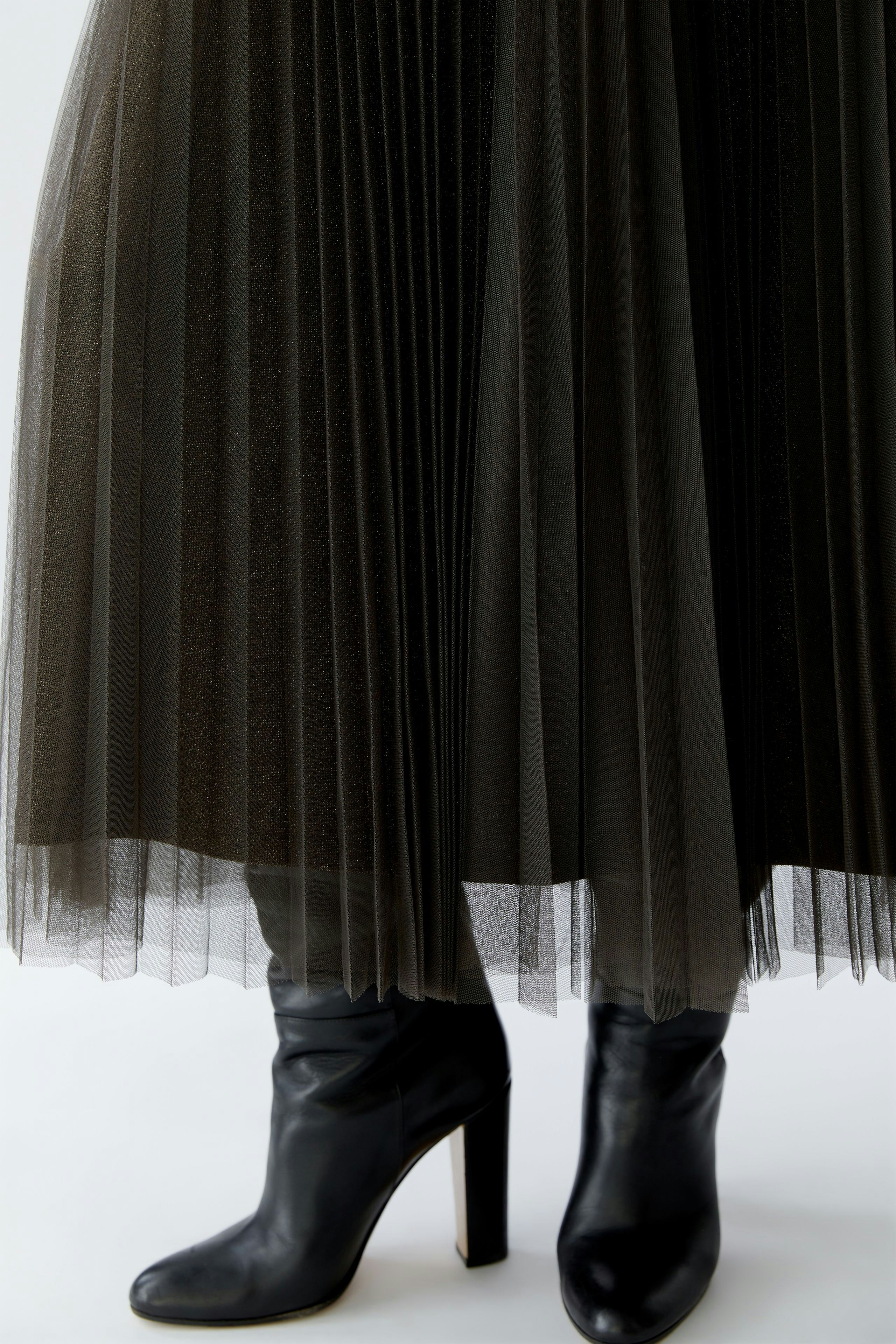 Pleated skirt: A woman wearing a flowing, dark pleated skirt paired with stylish black heeled boots.