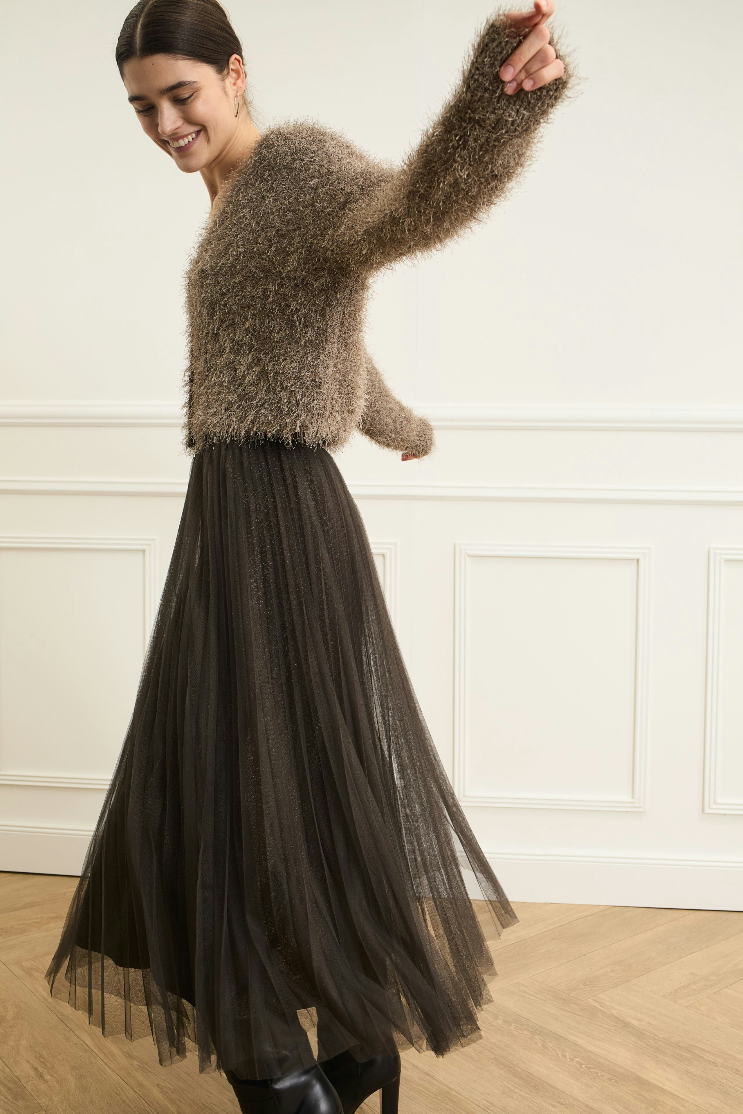 Flowy pleated skirt: Woman in a soft, fluffy pullover and a long, dark pleated skirt, dancing joyfully.