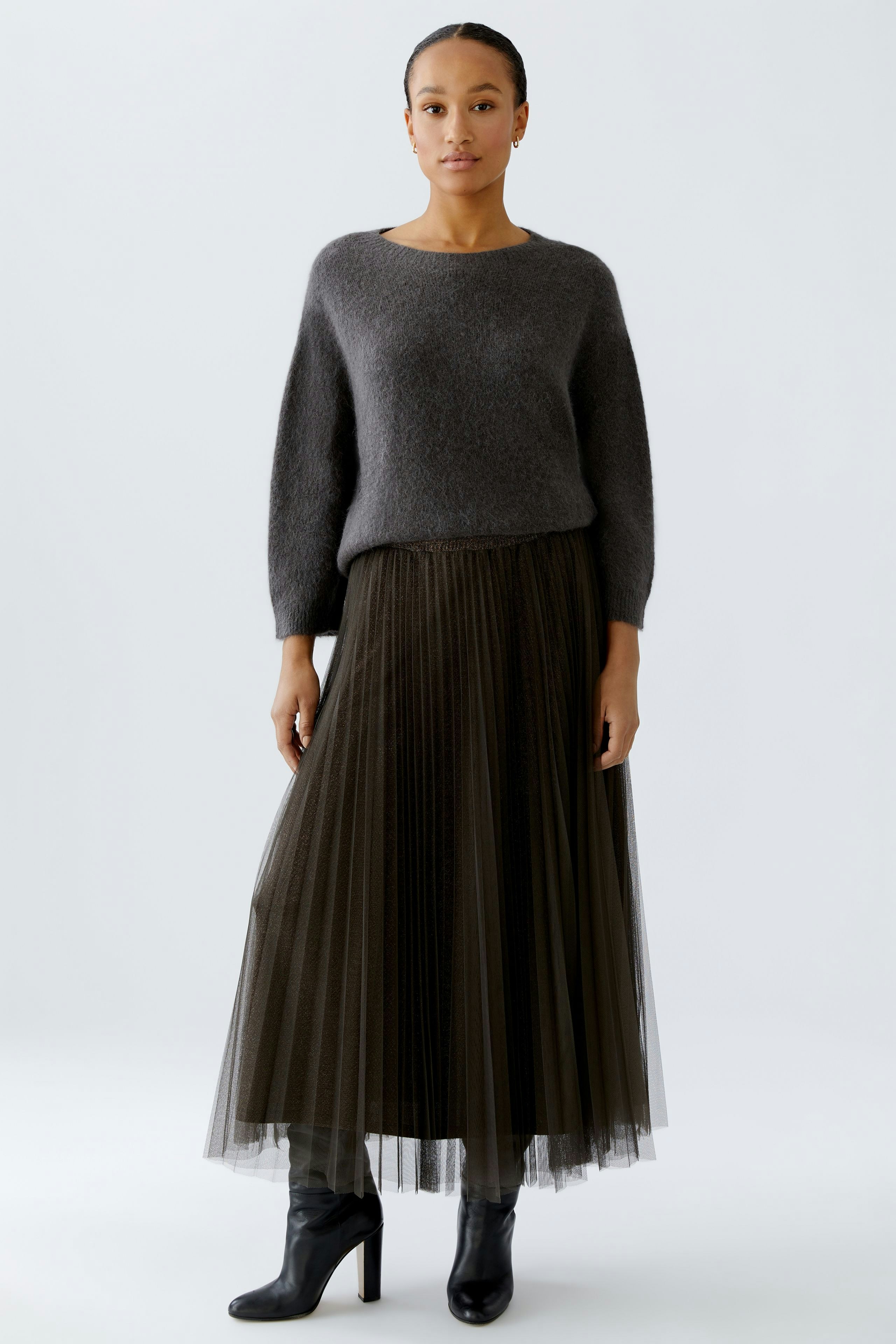 Modern pleated skirt: Woman in a dark pleated skirt paired with a cozy gray pullover.