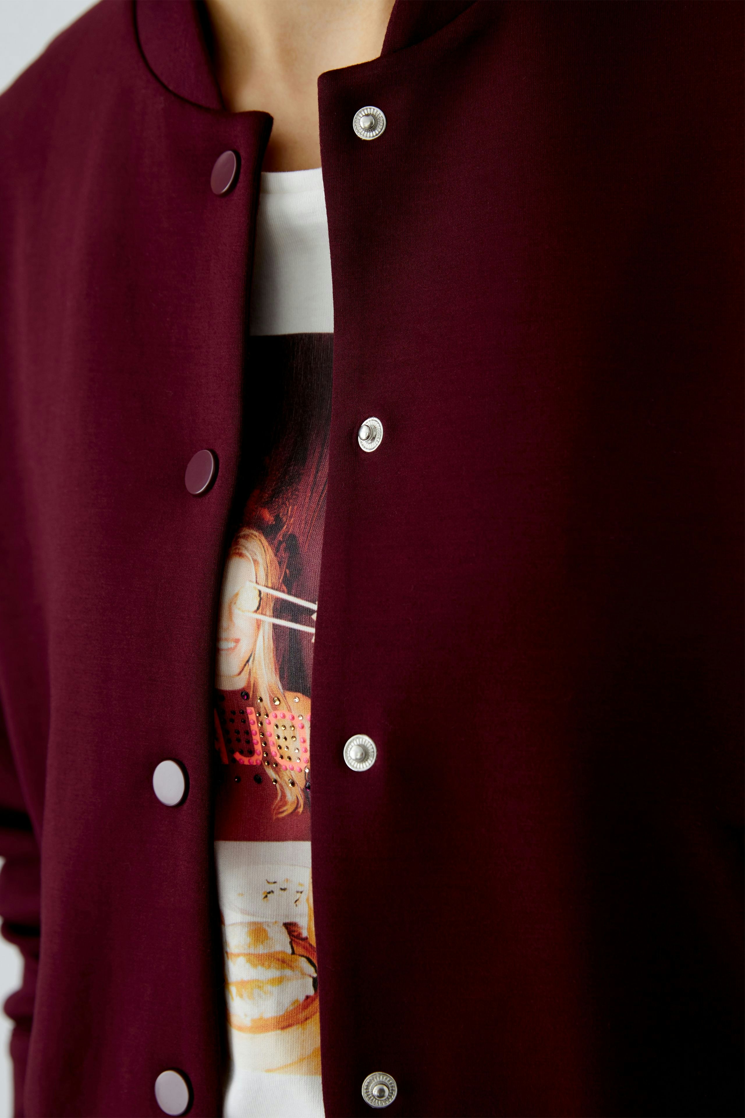 Casual women's blouson: Close-up of a woman in a burgundy jacket with snap buttons over a graphic tee.