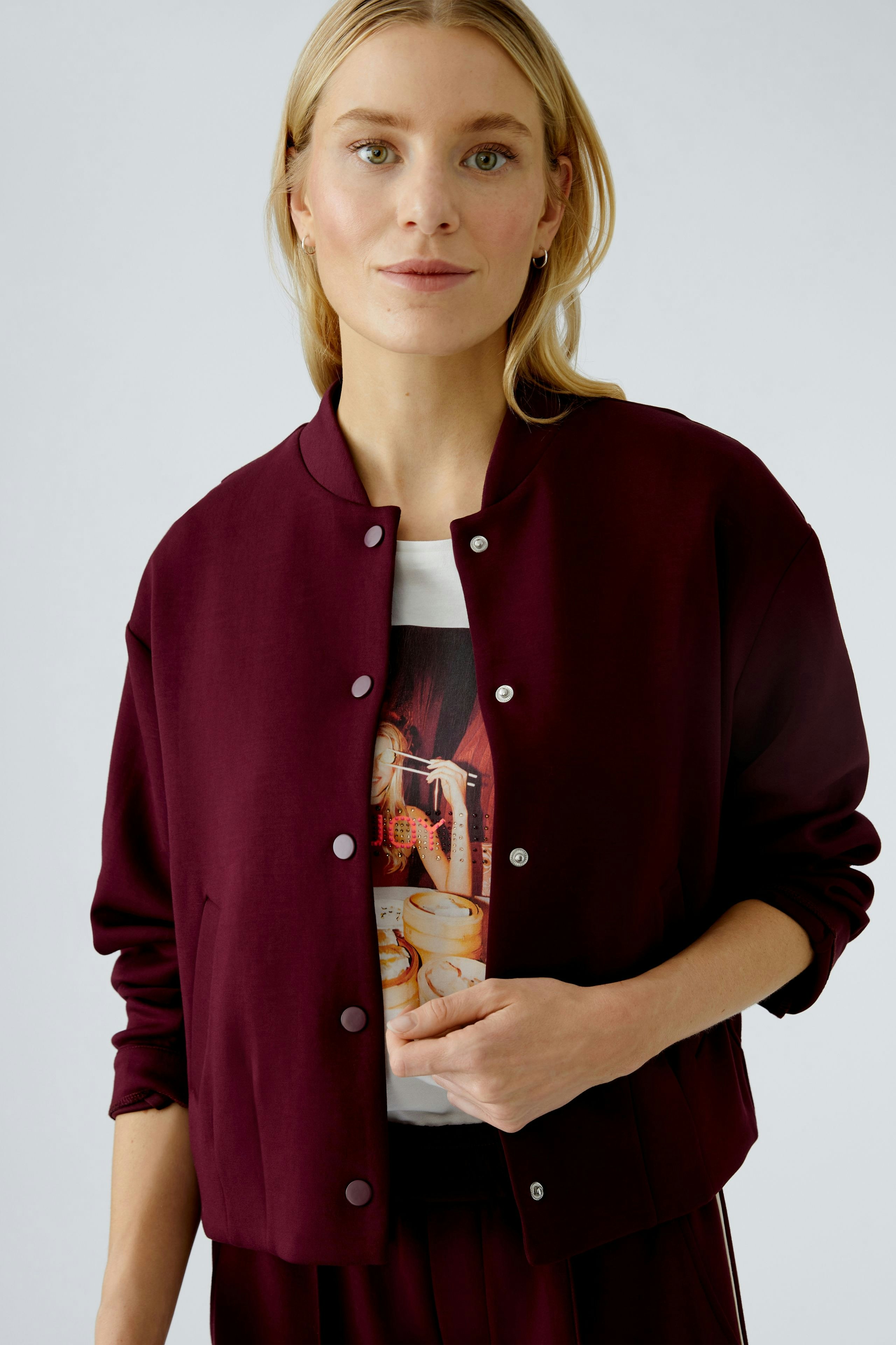 Casual women's blouson: Woman in a burgundy bomber jacket over a graphic tee, exuding a relaxed vibe.