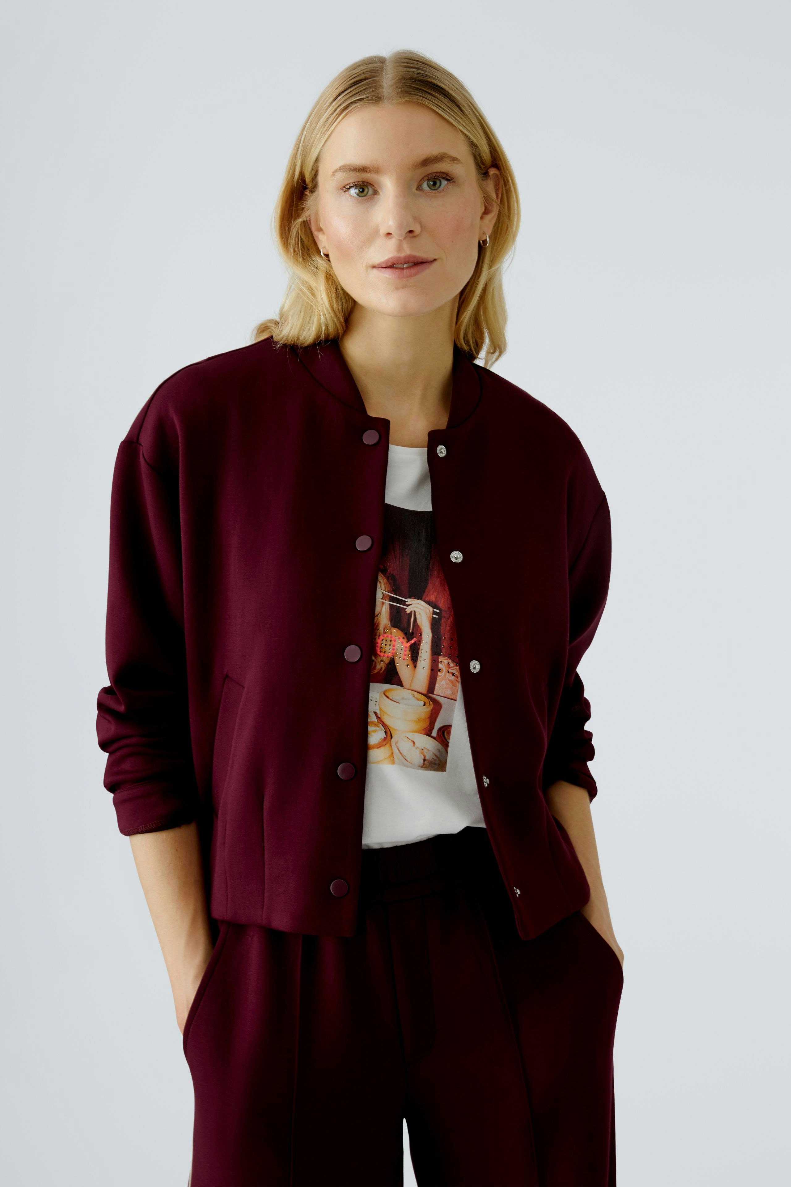 Casual women's blouson: A woman in a burgundy bomber jacket over a graphic tee, looking relaxed.