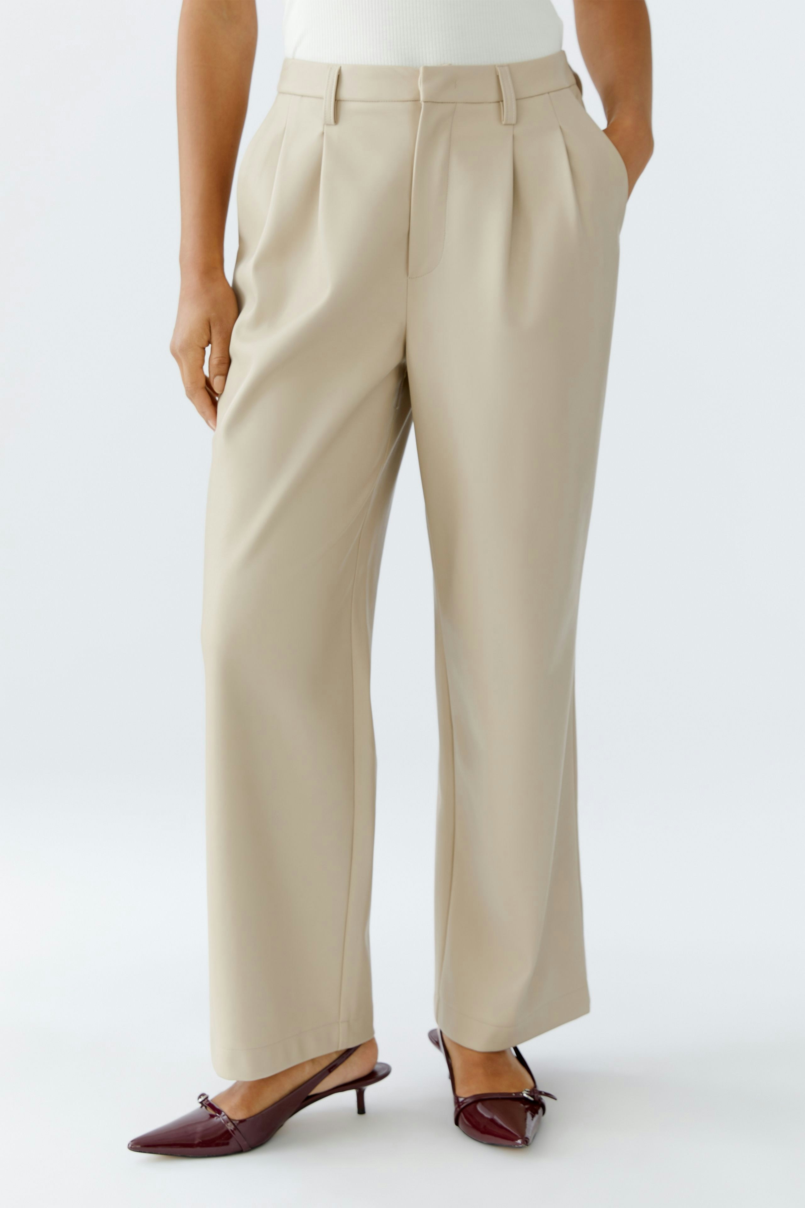 Chic women's pleated trousers in beige, styled with a fitted top and stylish shoes.