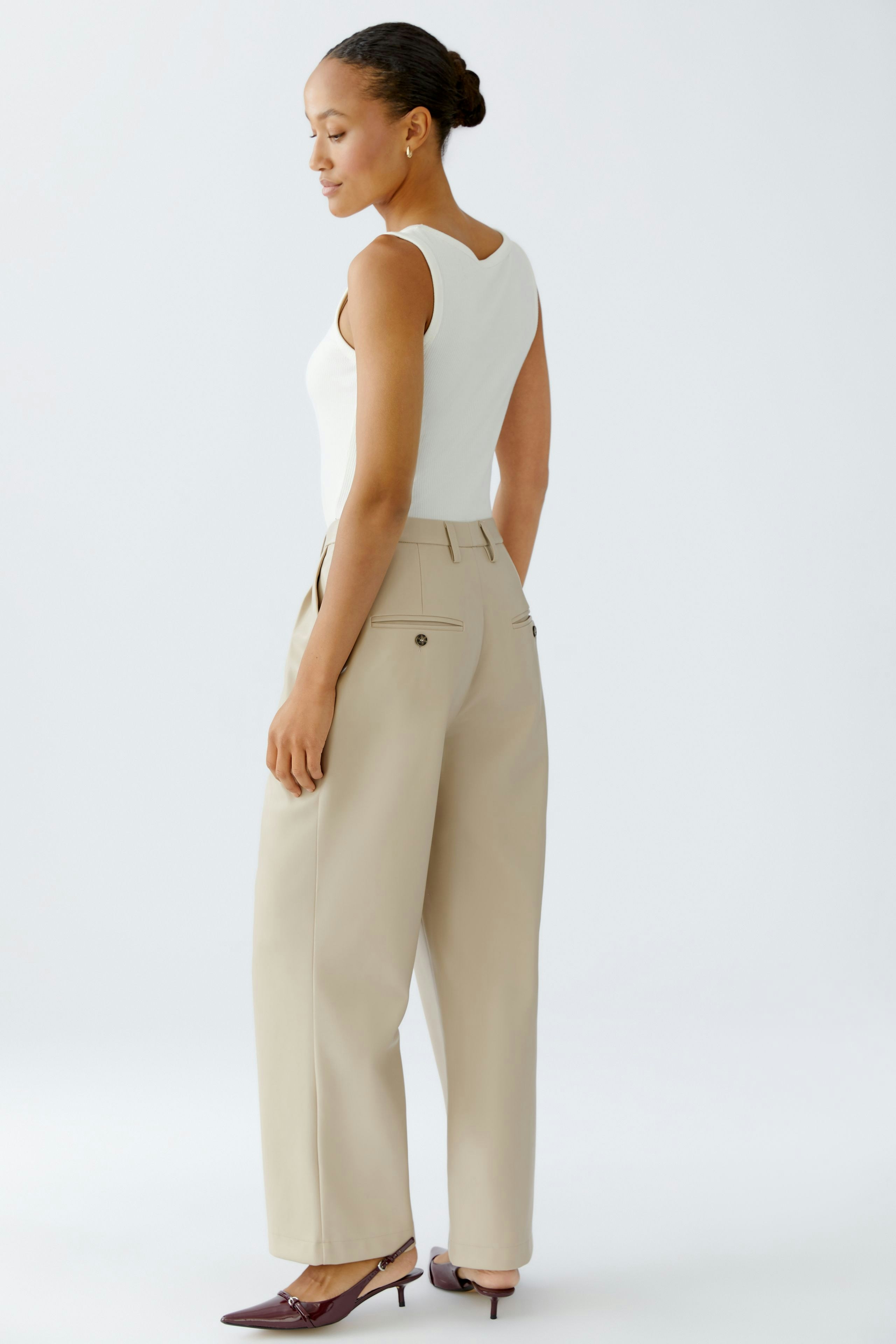 Casual women's pleated trousers: A woman in beige trousers with a fitted white top, showcasing a relaxed style.
