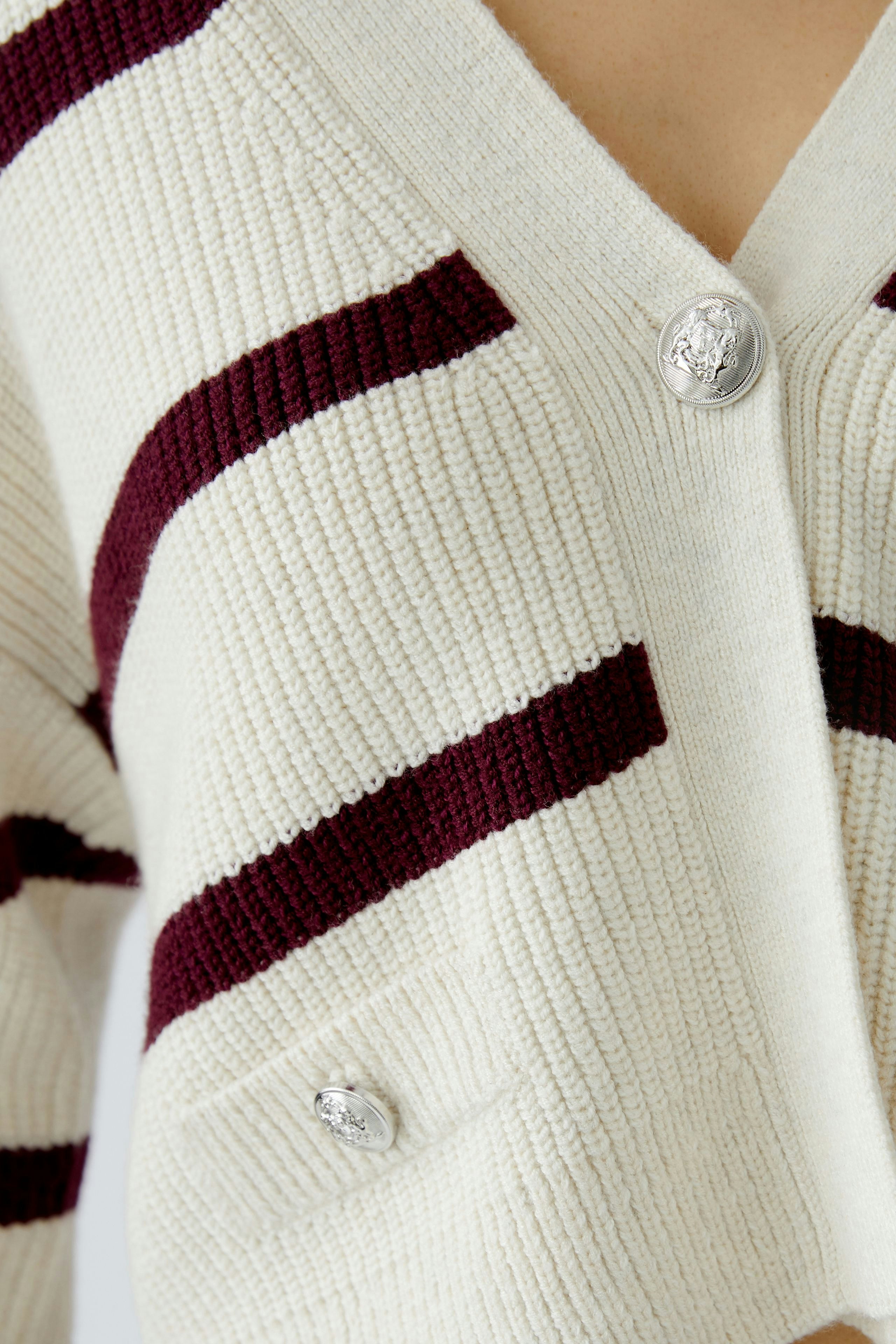 Casual women's cardigan: Close-up of a cream cardigan with maroon stripes and stylish buttons.