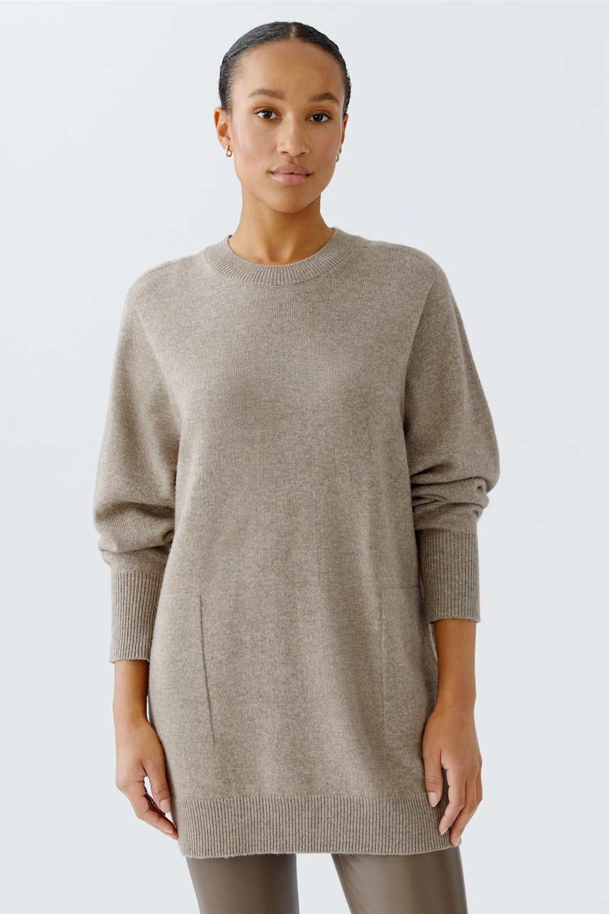 Bequemer Damen-Pullover in Beige mit lässigem Schnitt und praktischen Taschen, getragen von einer Frau.