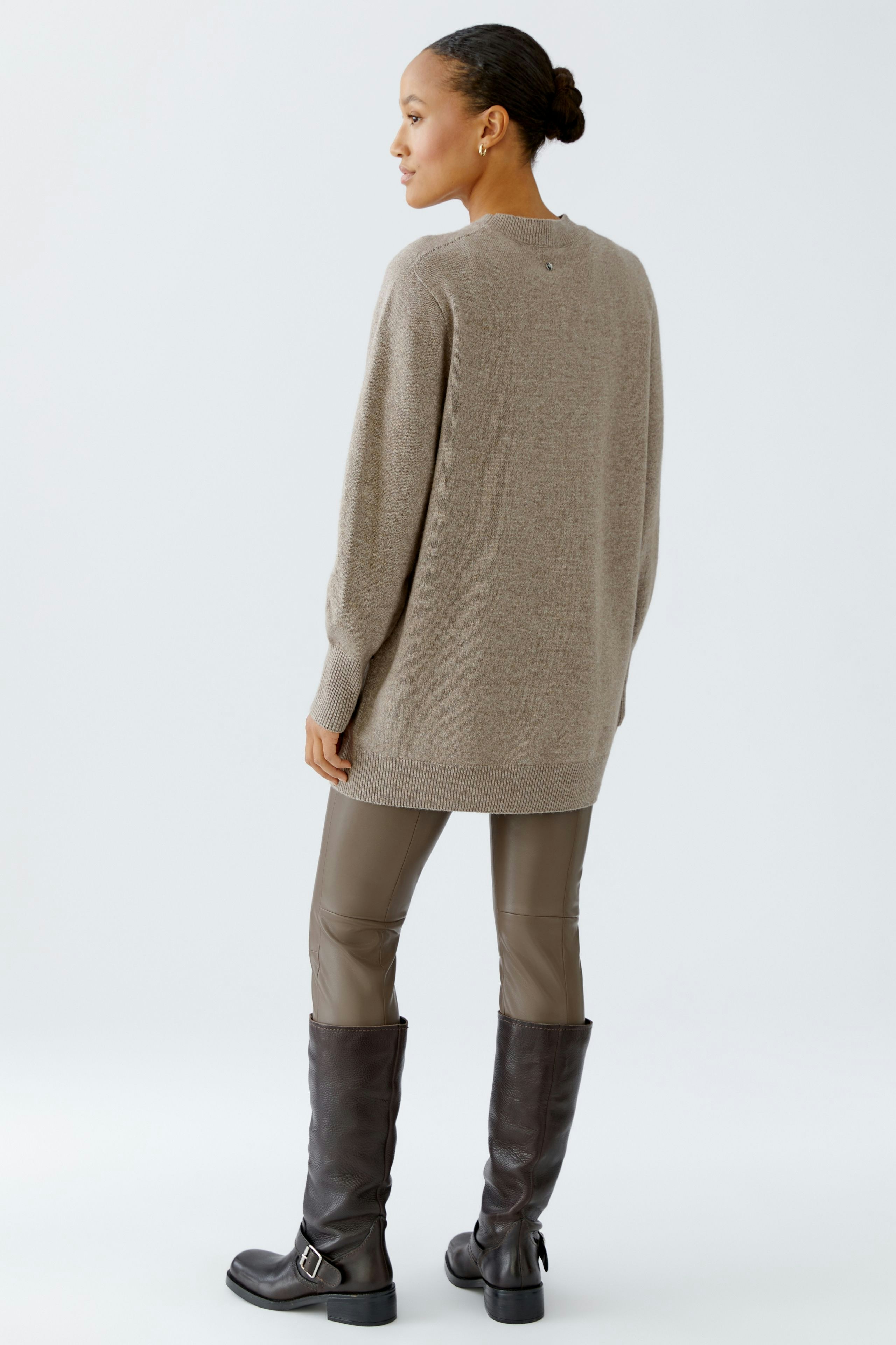 Casual women's pullover: A woman in a beige pullover paired with sleek leggings and tall boots.