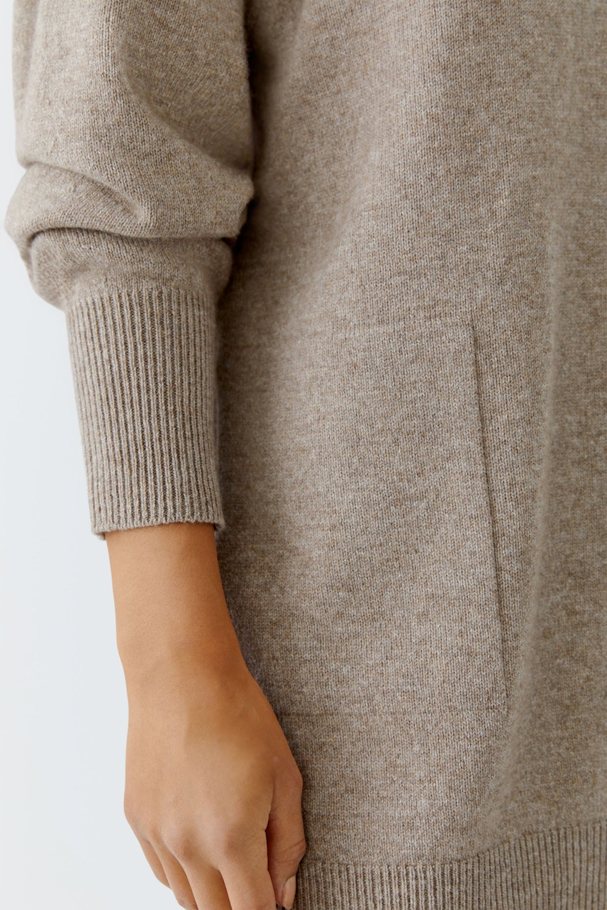 Beiger Damen-Pullover: Frau mit lässigem, weichem Strickpullover und praktischen Taschen.