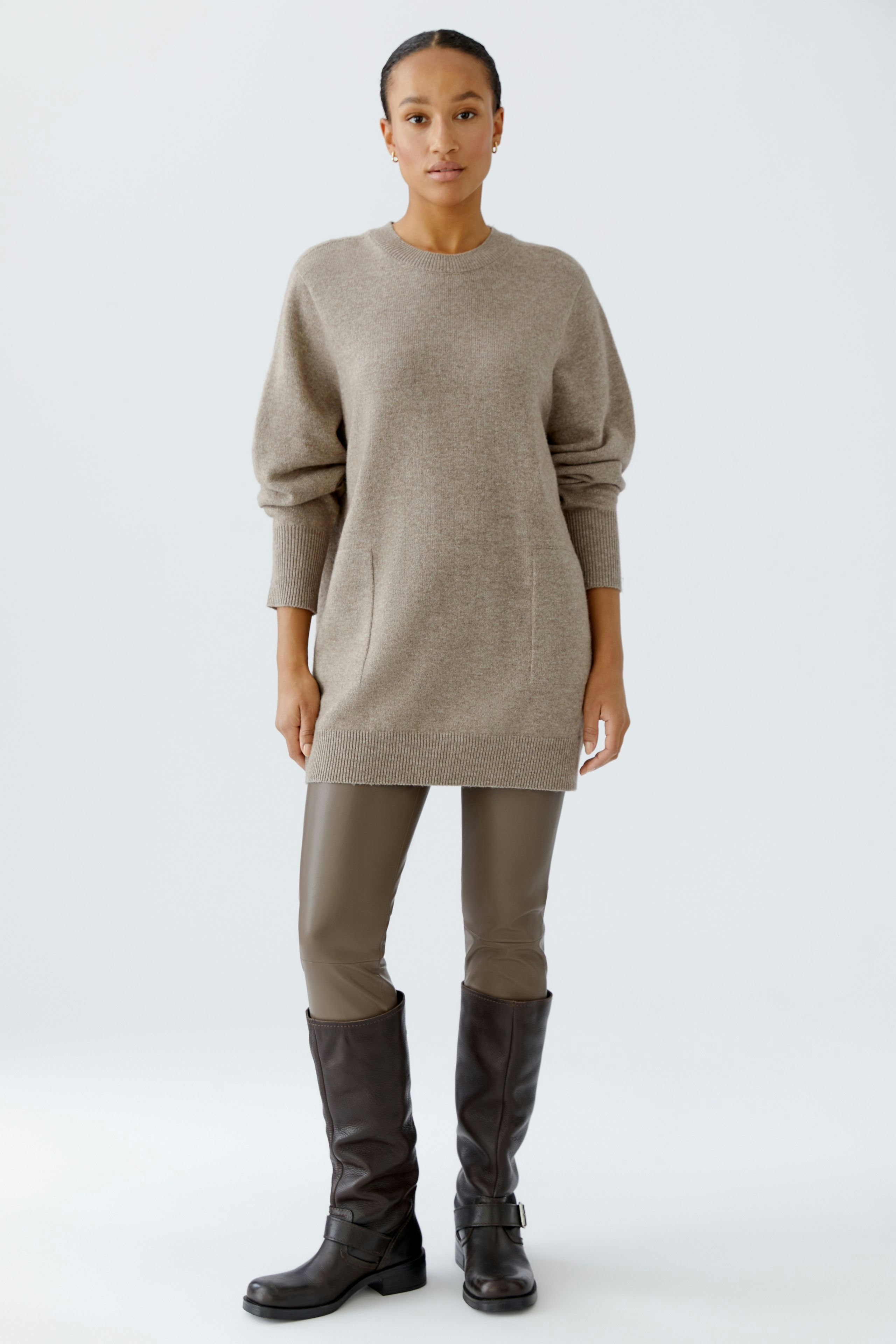 Casual women's pullover: A woman in a beige oversized pullover paired with fitted pants and knee-high boots.