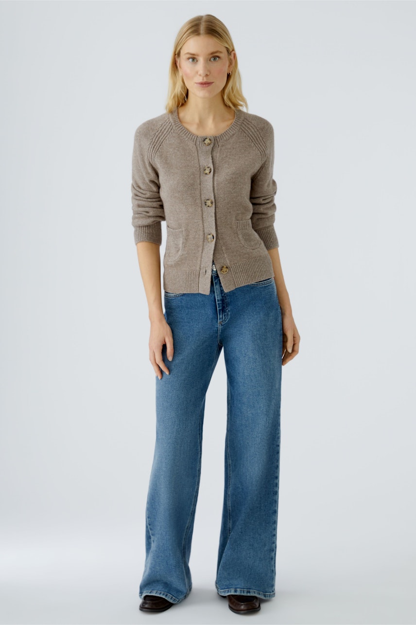 Damen-Strickjacke: Frau in beiger Strickjacke mit Knöpfen und lässigen Jeans steht entspannt.
