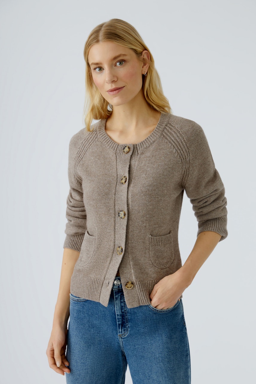 Beige Strickjacke: Frau trägt eine bequeme Strickjacke mit Knöpfen und Taschen, kombiniert mit Jeans.