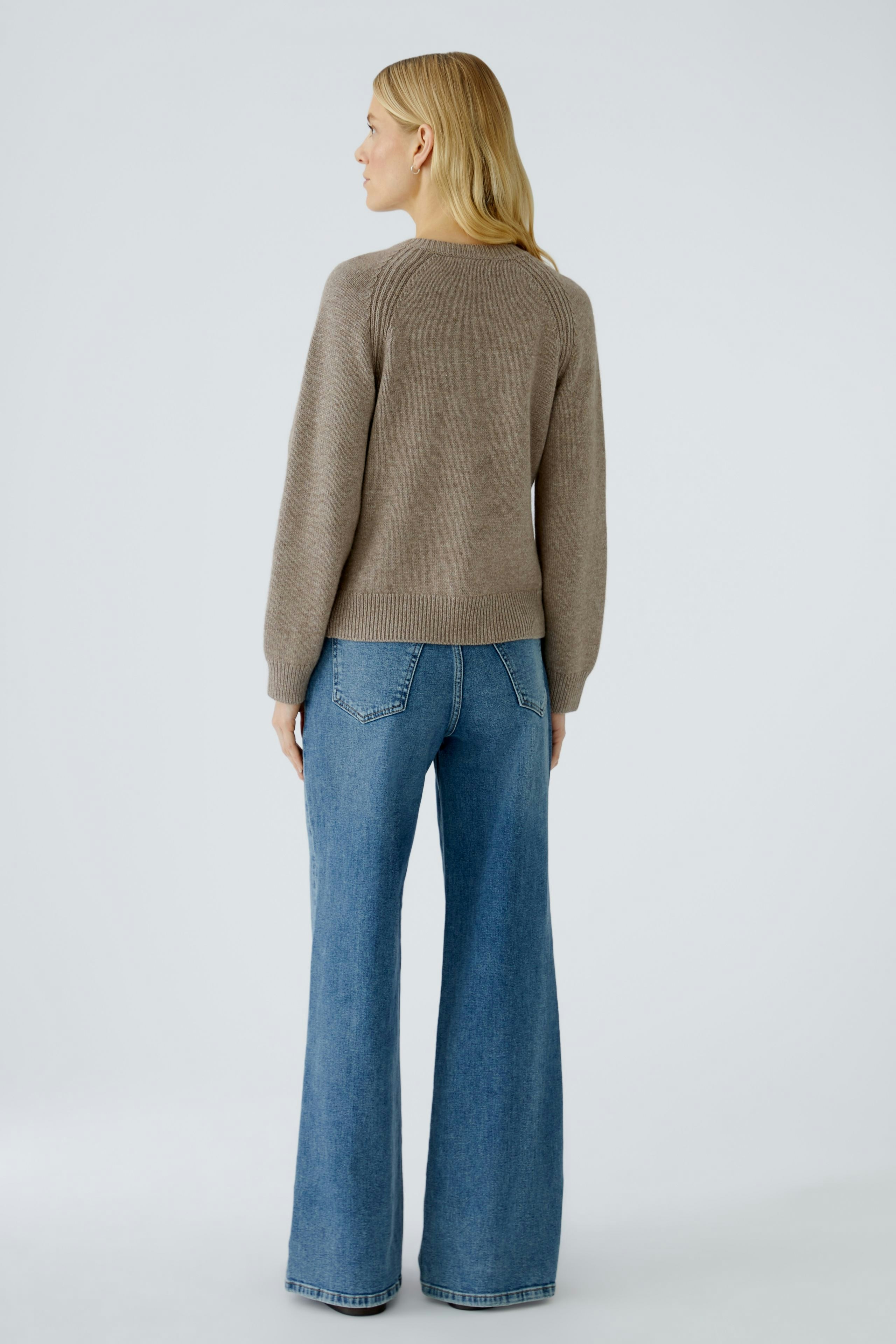 Casual women's cardigan: A woman in a cozy brown pullover, paired with flared jeans, showcasing a relaxed style.