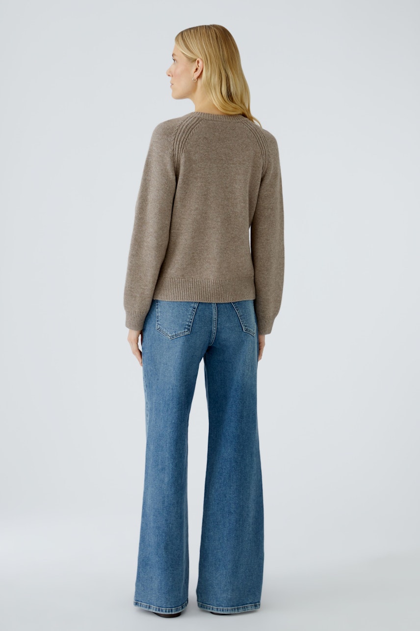 Bequeme Damen-Strickjacke: Frau mit brauner Strickjacke und lässigen Jeans von hinten.