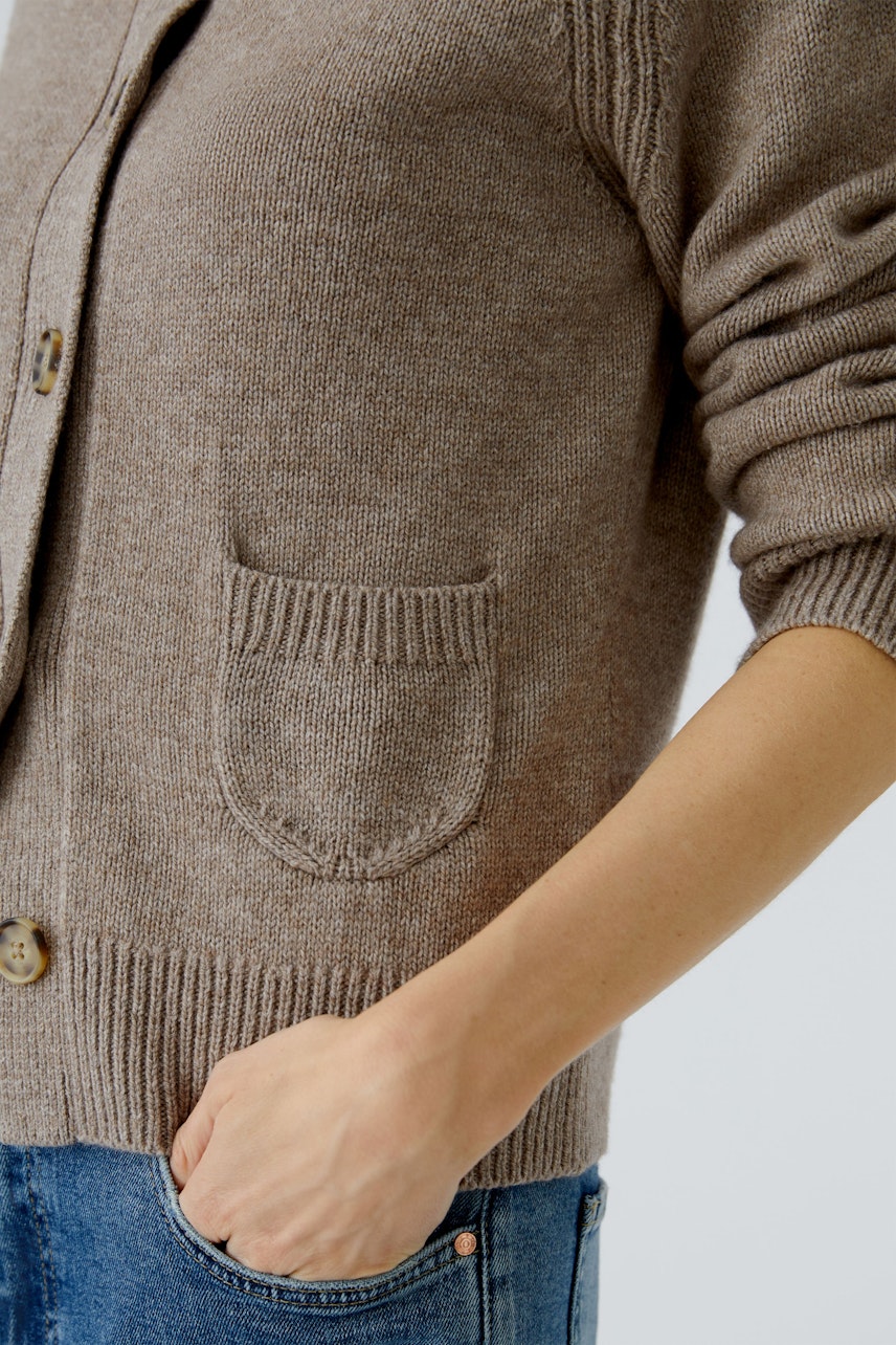 Beige Strickjacke: Frau trägt eine gemütliche Strickjacke mit Taschen und Knöpfen, ideal für den Alltag.