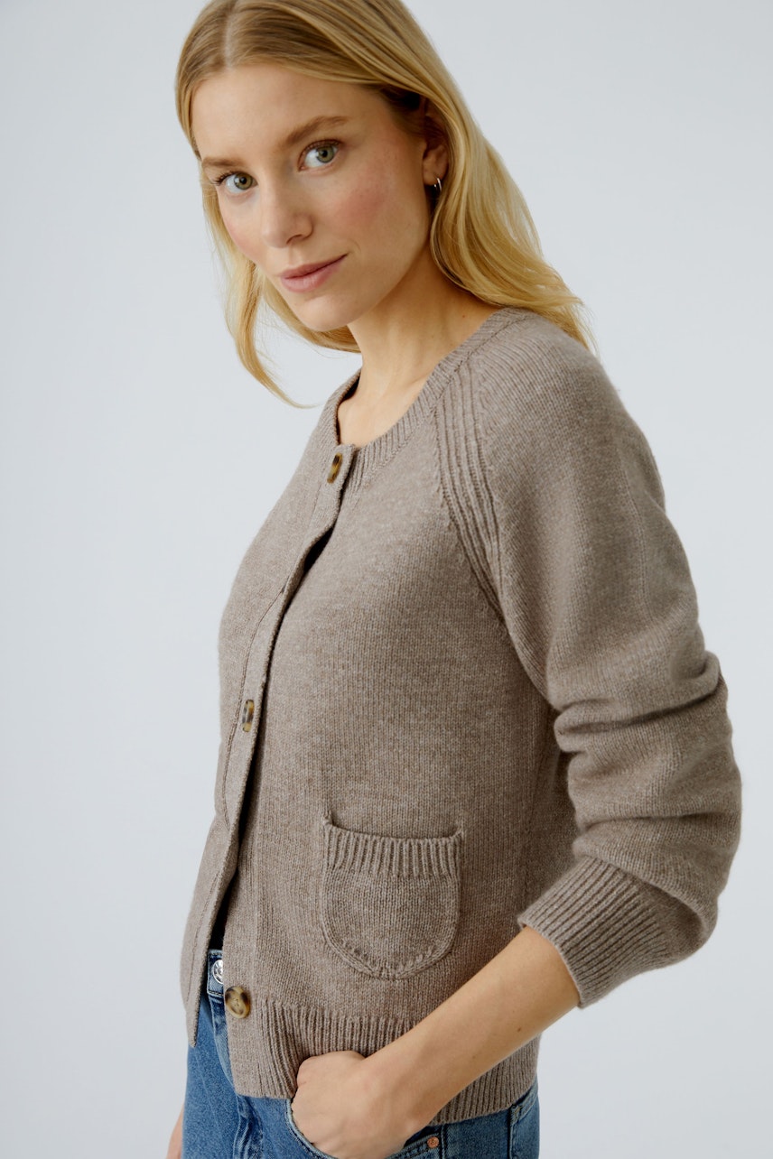 Beige Strickjacke: Frau in lässiger Strickjacke mit Knöpfen und Taschen, kombiniert mit Jeans.