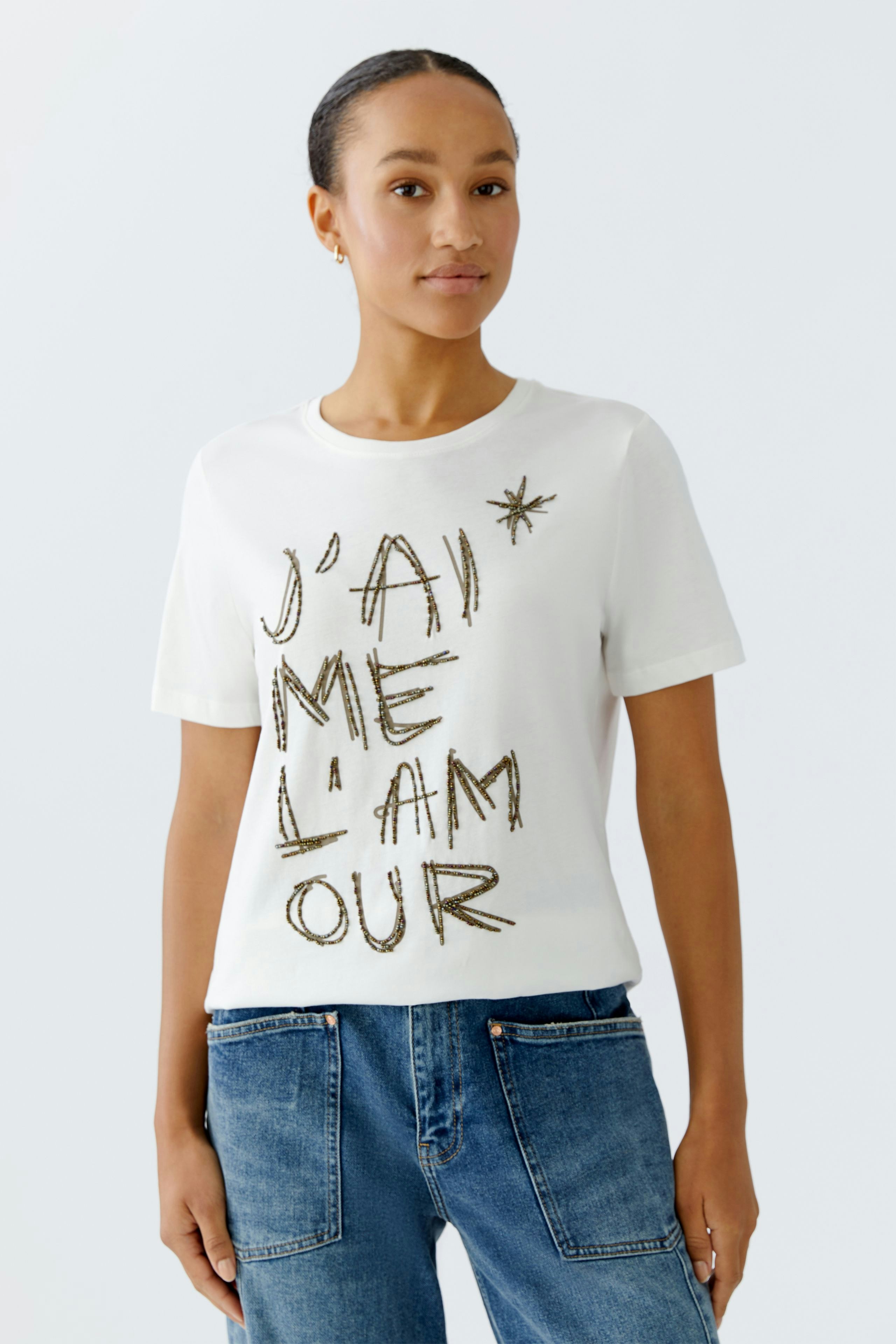 Damen-T-Shirt: Junge Frau trägt ein weißes Shirt mit goldener Schrift und lässigen Jeans.