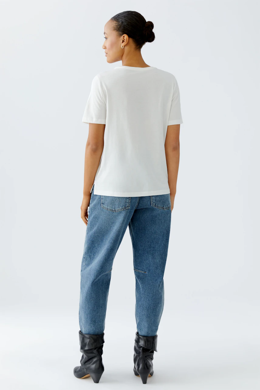 Casual women's t-shirt: A woman in a white t-shirt and relaxed jeans stands confidently.