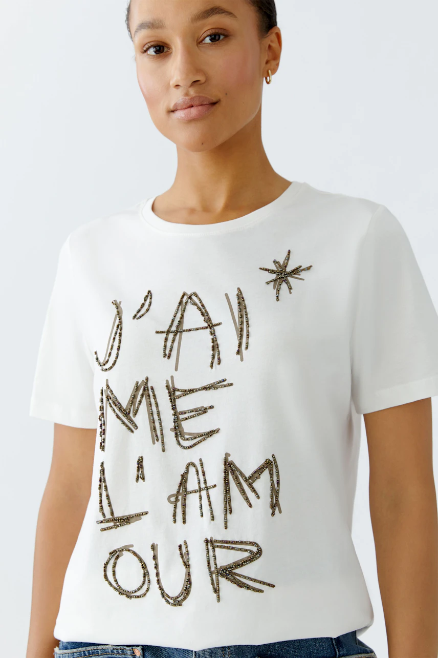 Casual women's t-shirt: Young woman in a white shirt with a graphic print, smiling confidently.