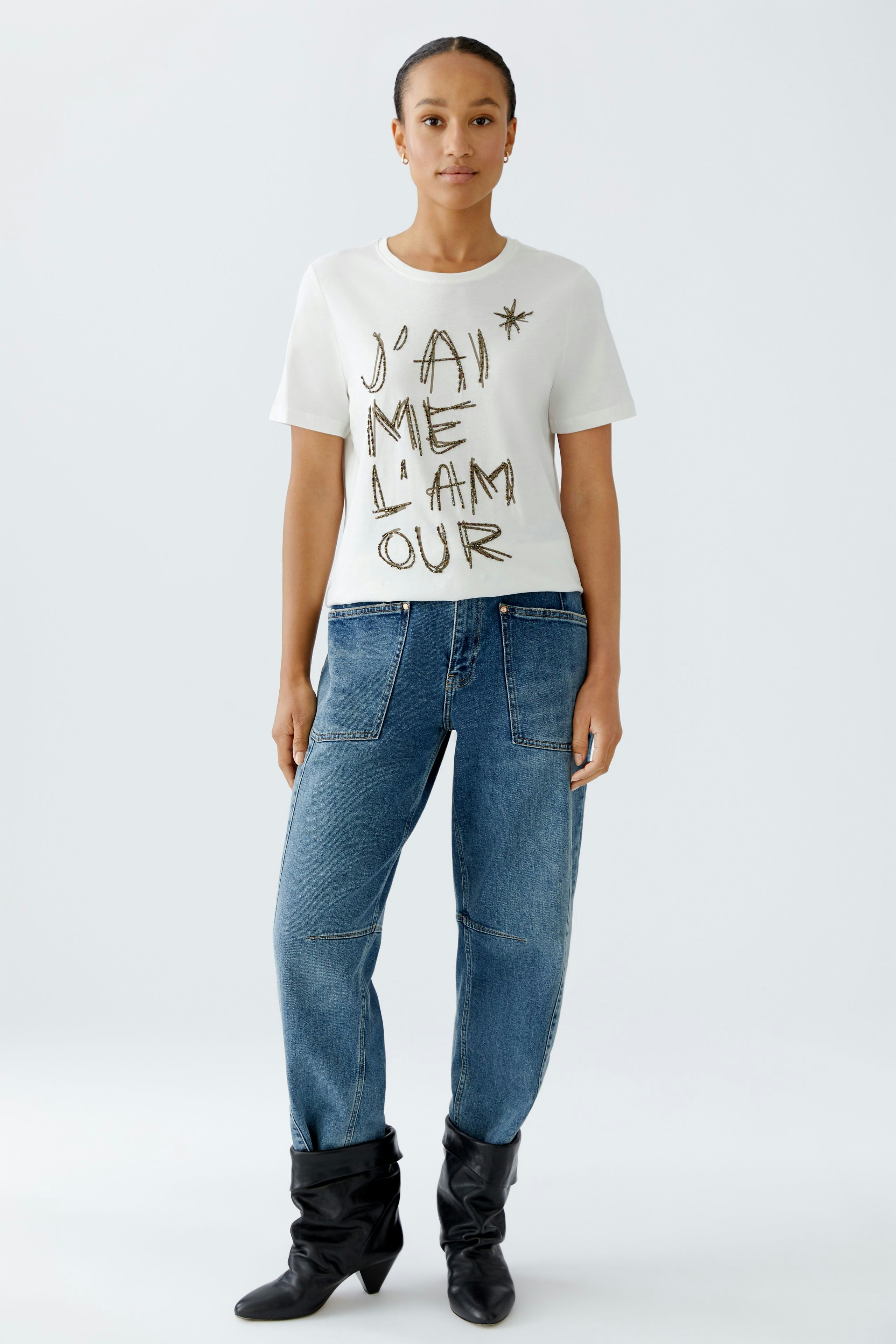 Damen-T-Shirt: Frau trägt ein weißes Shirt mit auffälligem Schriftzug und lässigen Jeans.