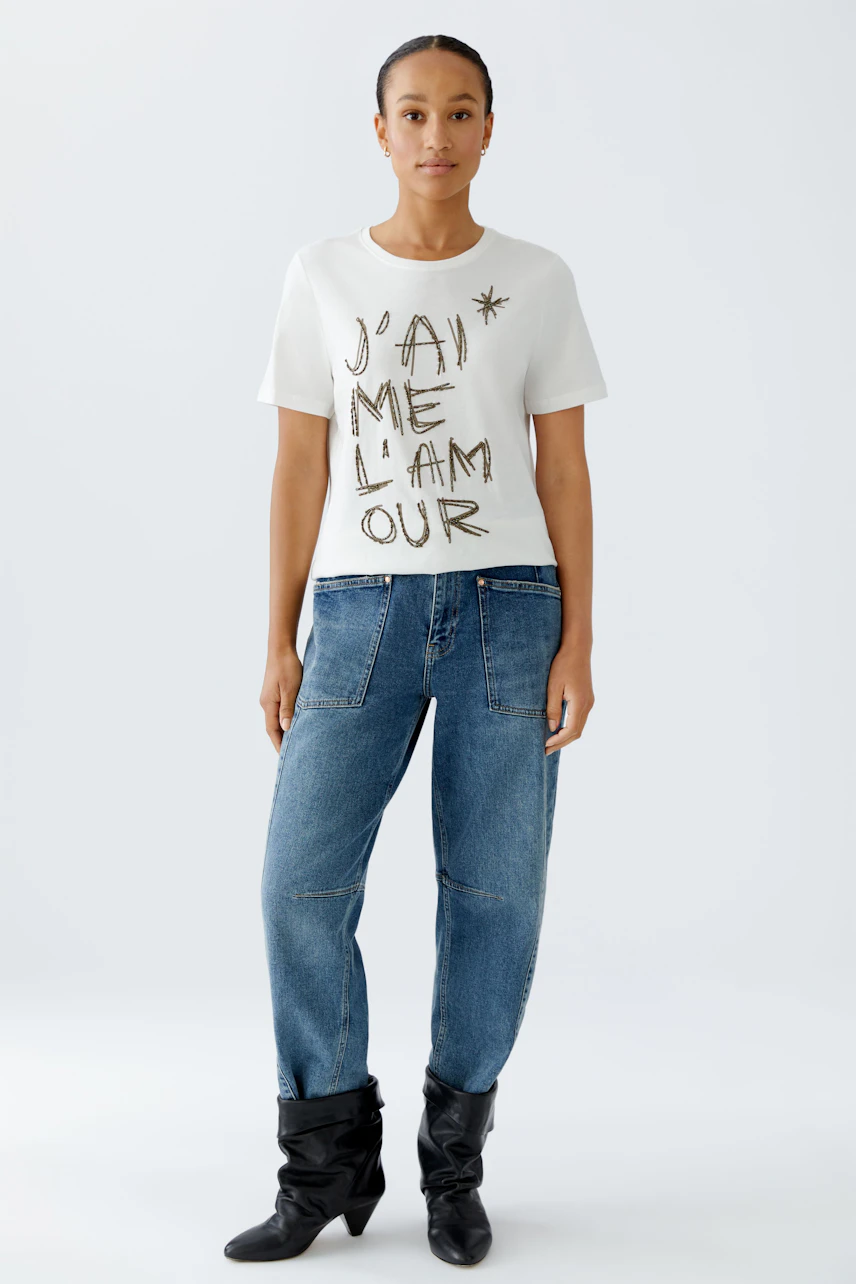 Casual women's t-shirt: Young woman in a white shirt with bold lettering and relaxed jeans.