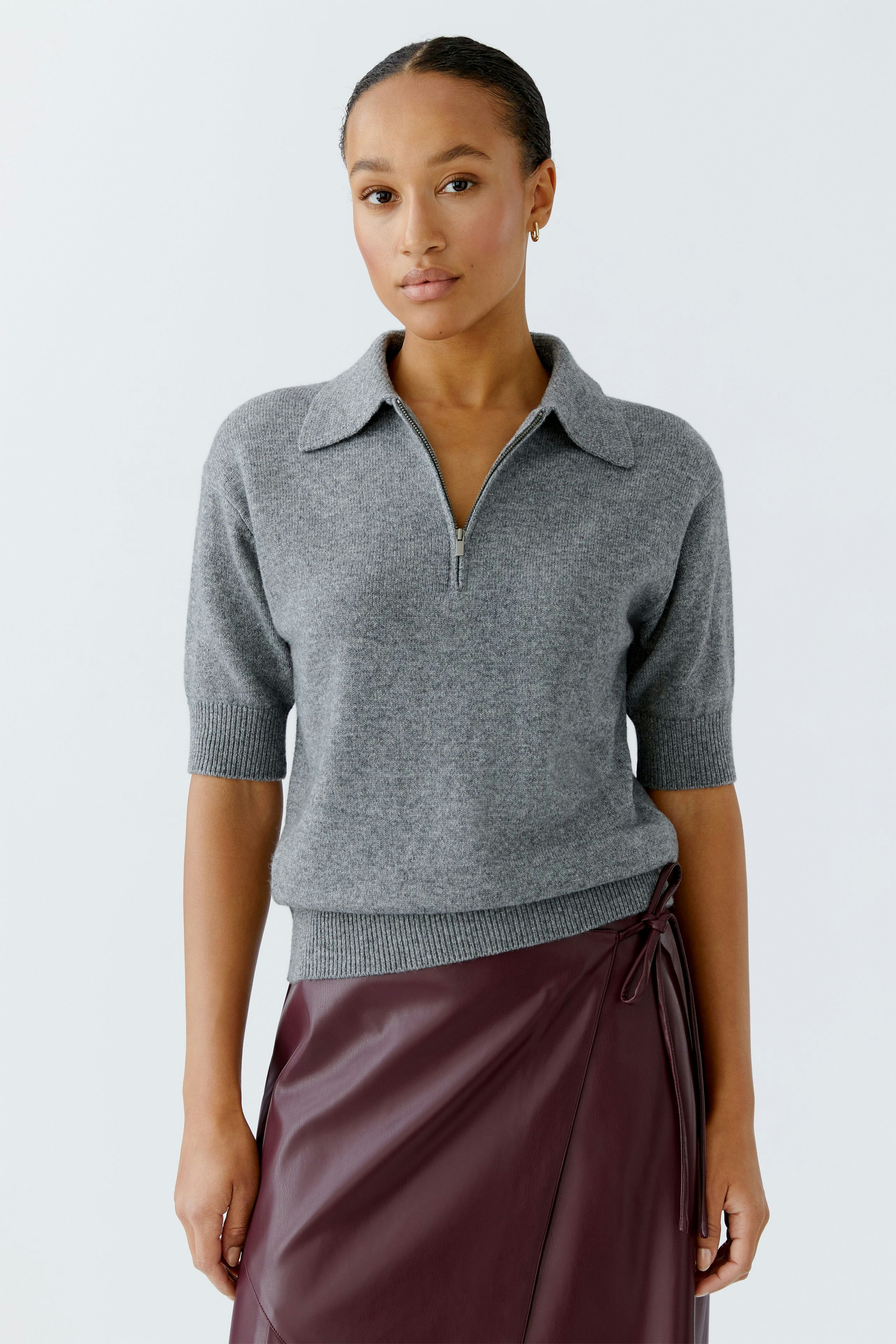 Damen-Pullover: Junge Frau in grauem Pullover mit kurzem Reißverschluss und lässigem Schnitt.