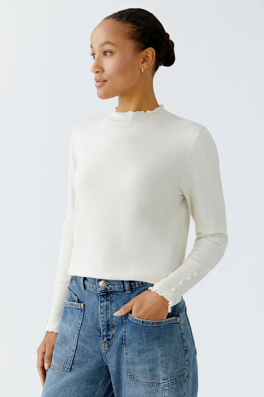 Damen-Pullover: Frau in cremefarbenem Pullover mit Rüschensaum und Knöpfen, kombiniert mit lässigen Jeans.