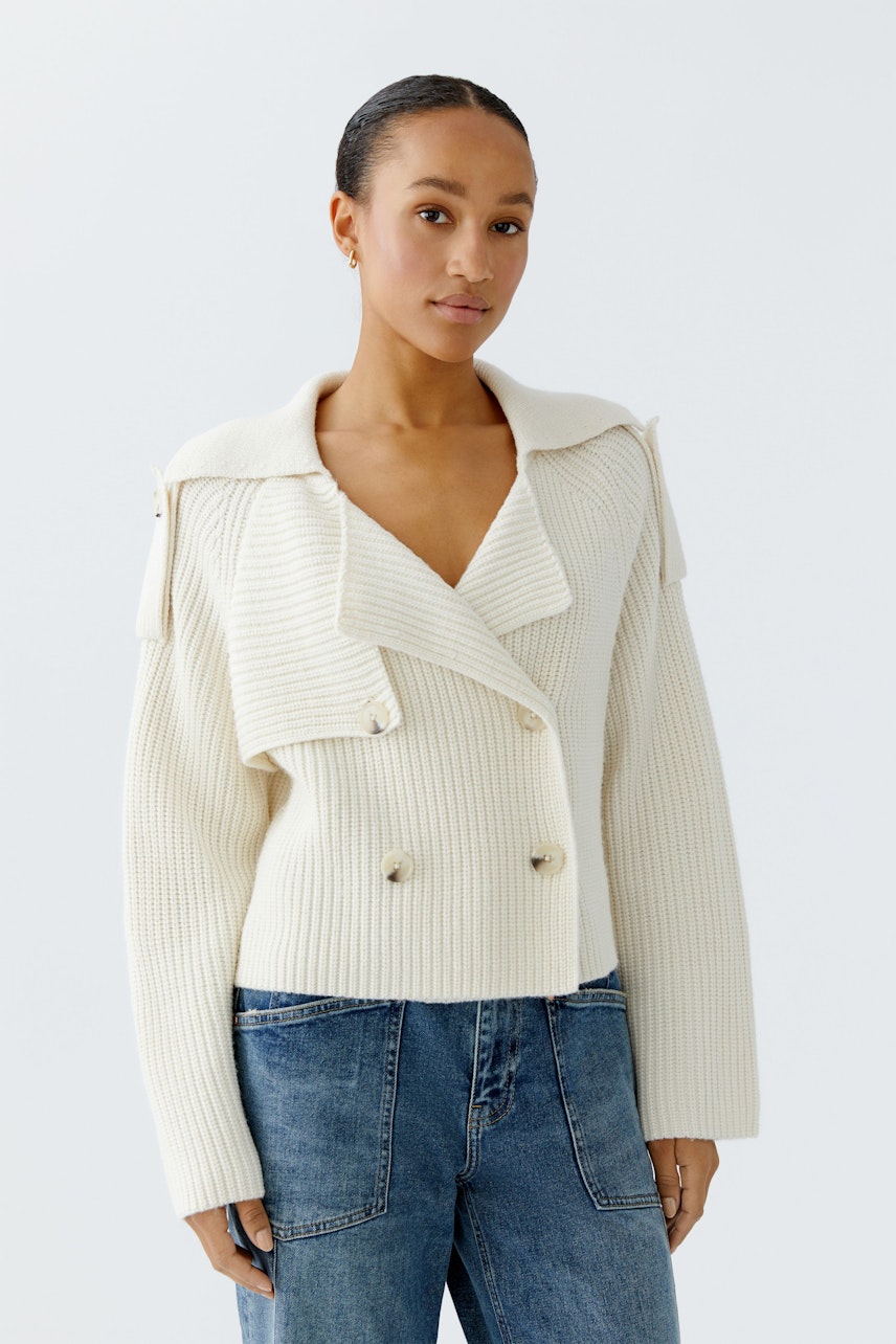 Moderne Damen-Strickjacke: Frau in cremefarbener Strickjacke mit breitem Kragen und Knöpfen.