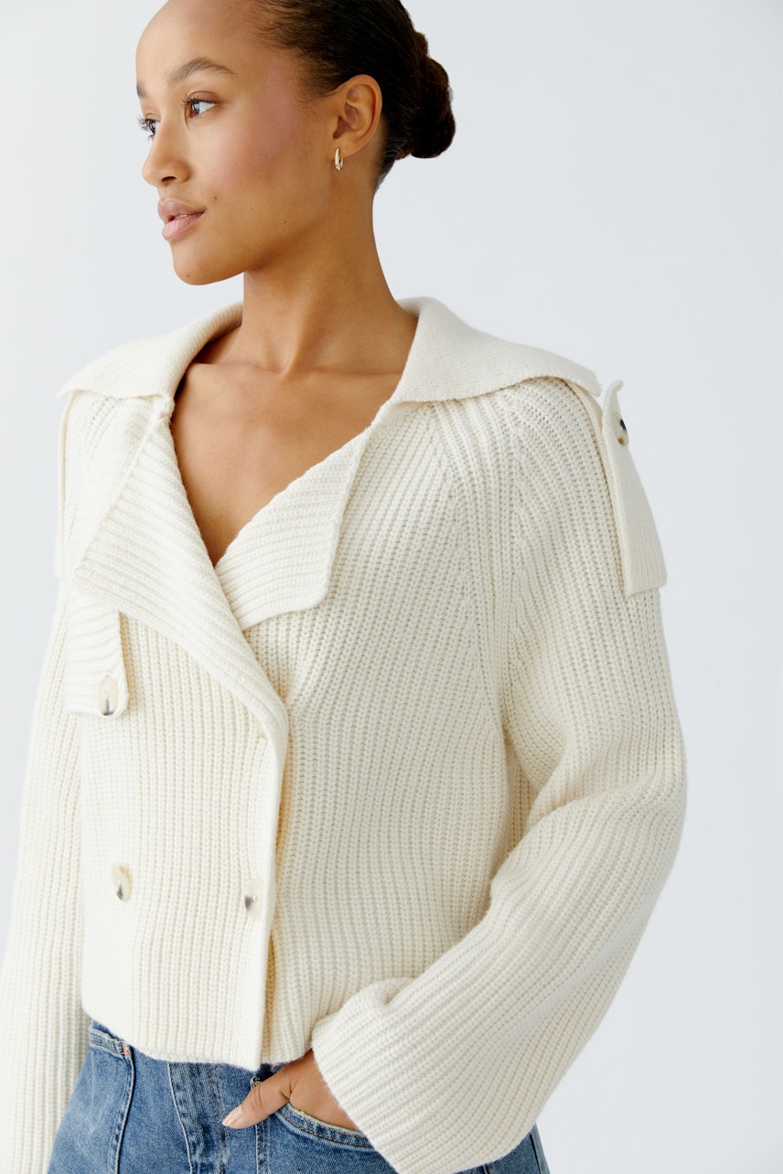 Moderne Damen-Strickjacke: Frau in cremefarbener Strickjacke mit breitem Kragen und lässigem Schnitt.