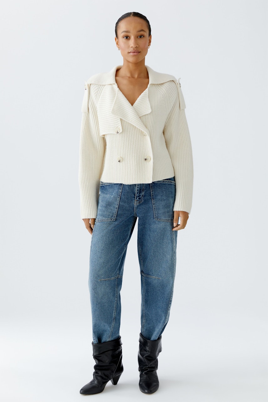 Moderne Damen-Strickjacke: Frau in cremefarbener Strickjacke mit breitem Kragen und lässigen Jeans.