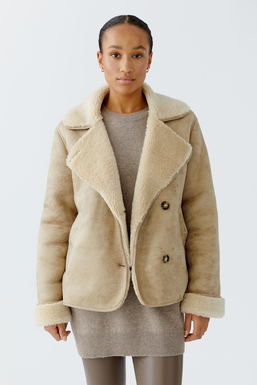 Beige Outdoorjacke: Frau trägt eine weiche Jacke mit großem Kragen und Knöpfen, ideal für kühle Tage.