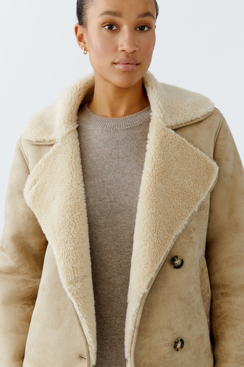 Damen-Outdoorjacke: Frau trägt eine beige Jacke mit weichem Kragen und Knöpfen.
