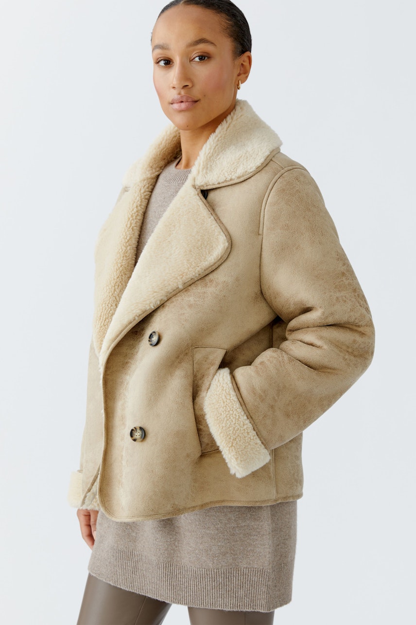 Beige Outdoorjacke: Frau trägt eine kuschelige Jacke mit Schafswollkragen und Knöpfen.