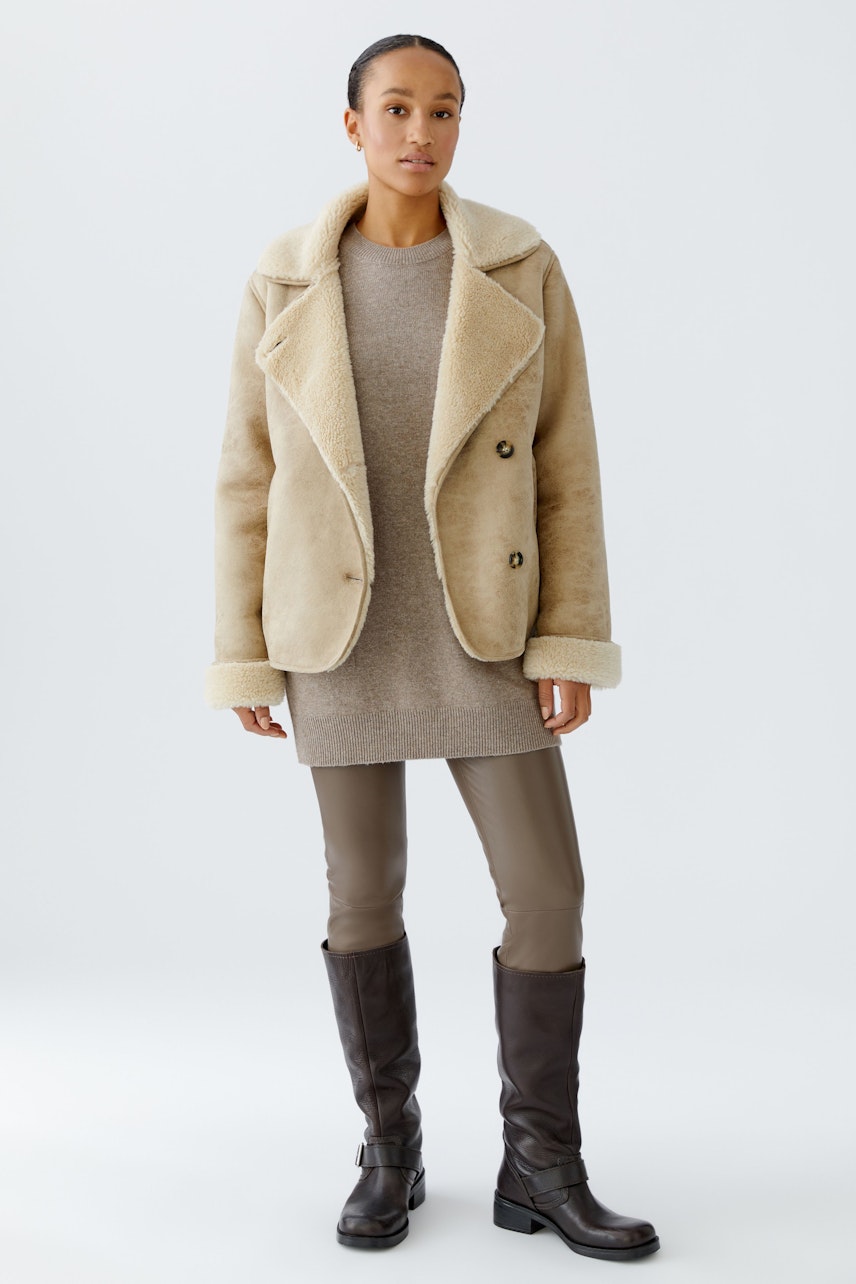 Beige Outdoorjacke: Frau trägt eine kuschelige Jacke mit breitem Kragen über einem grauen Kleid.