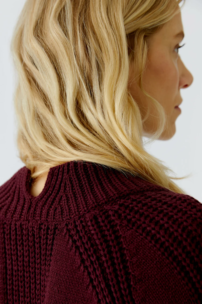 Damen-Pullover: Frau mit blonden Haaren trägt einen burgunderfarbenen Strickpullover mit strukturiertem Muster.