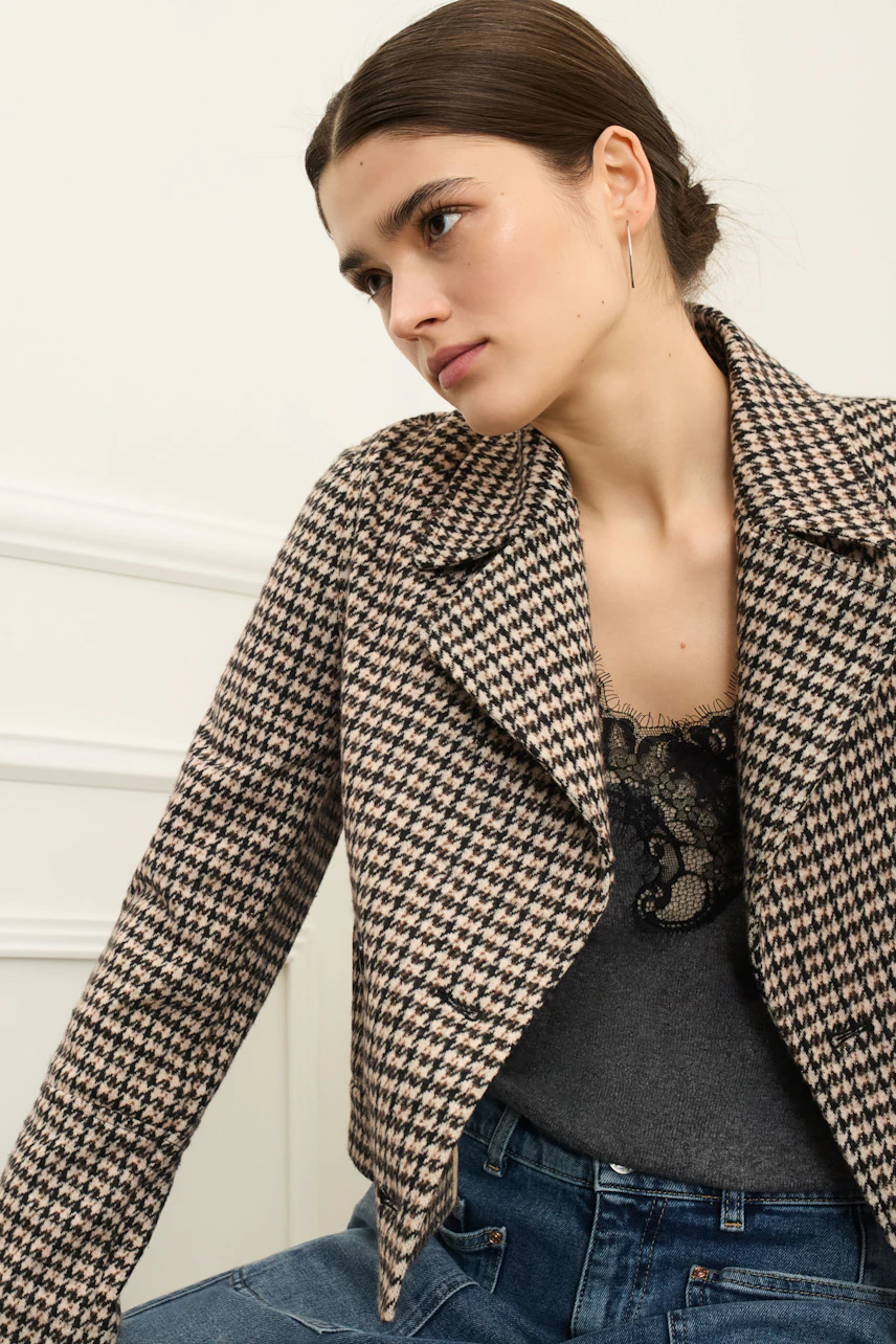 Stylish women's jacket: A woman in a checkered jacket over a lace top, paired with casual jeans.
