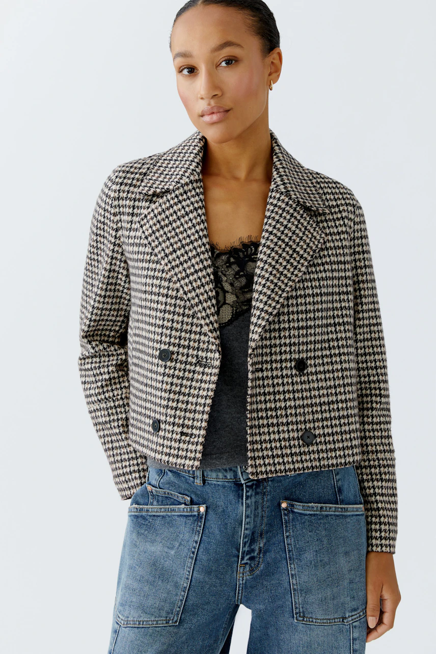 Stylish women's jacket: A woman in a checkered cropped jacket over a black top and denim pants.