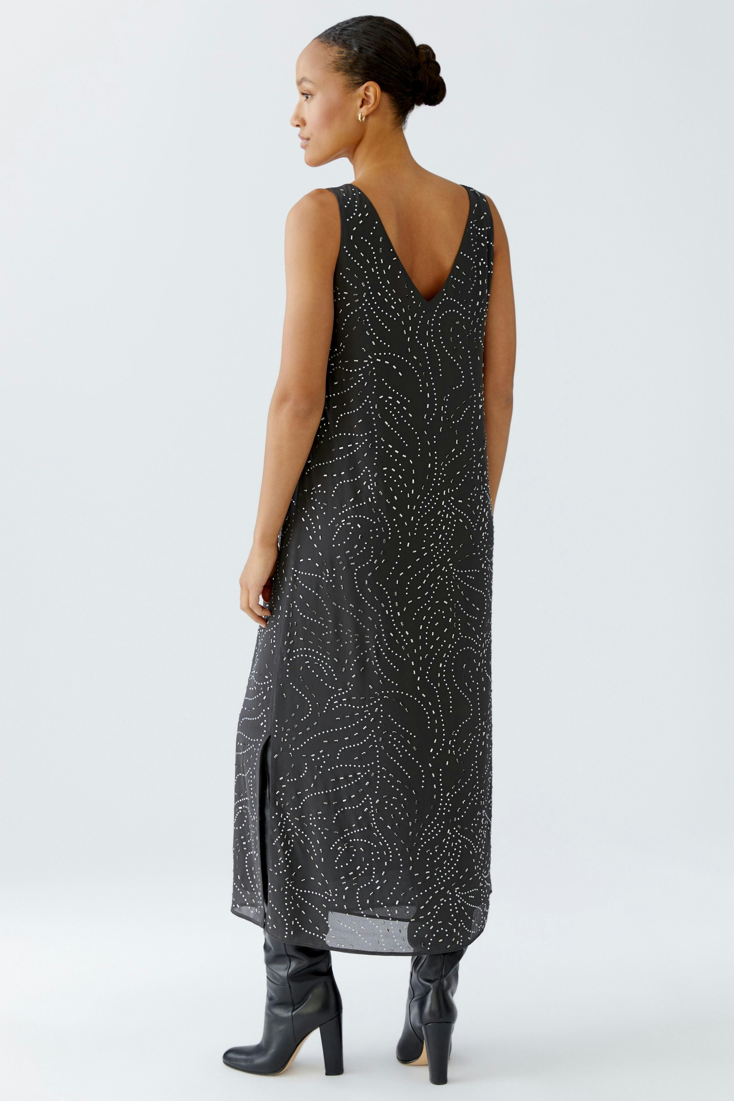 Sleeveless dress: Woman in a black dress with a V-neck and white patterns, paired with stylish boots.