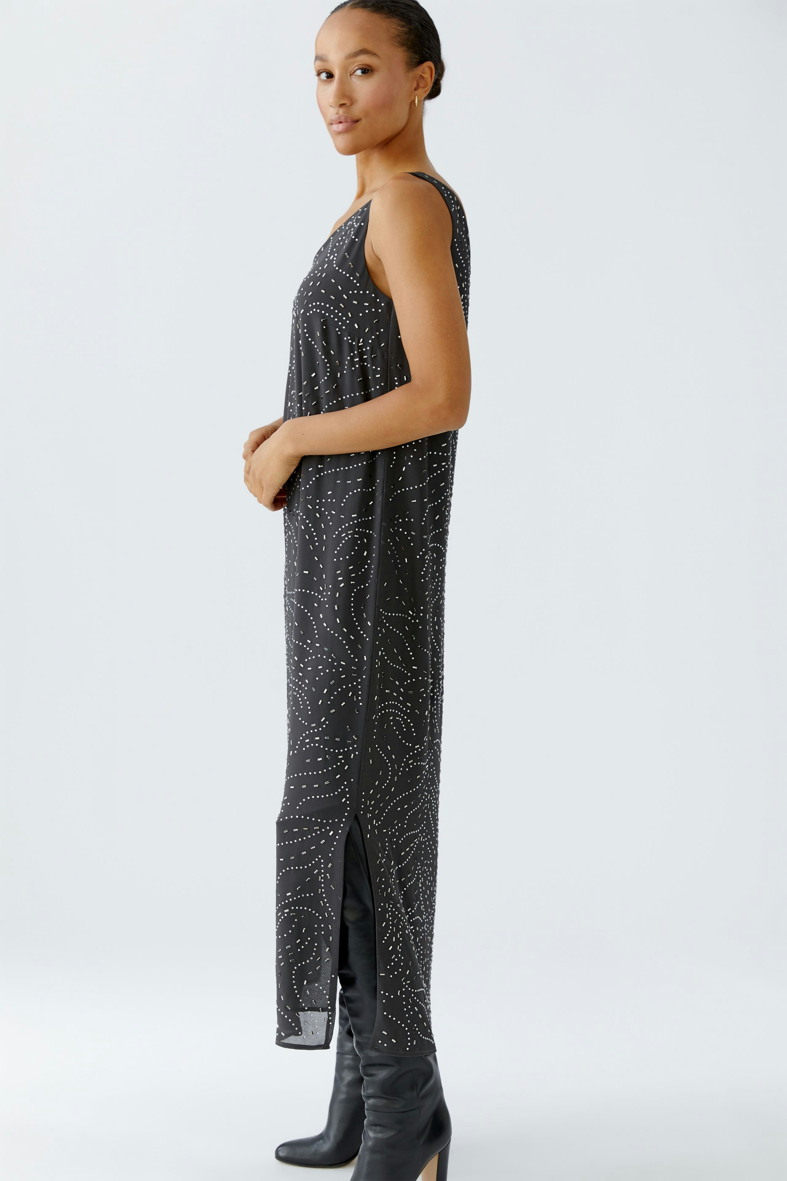 Casual women's dress: A woman in a black sleeveless dress with a subtle pattern and side slits.