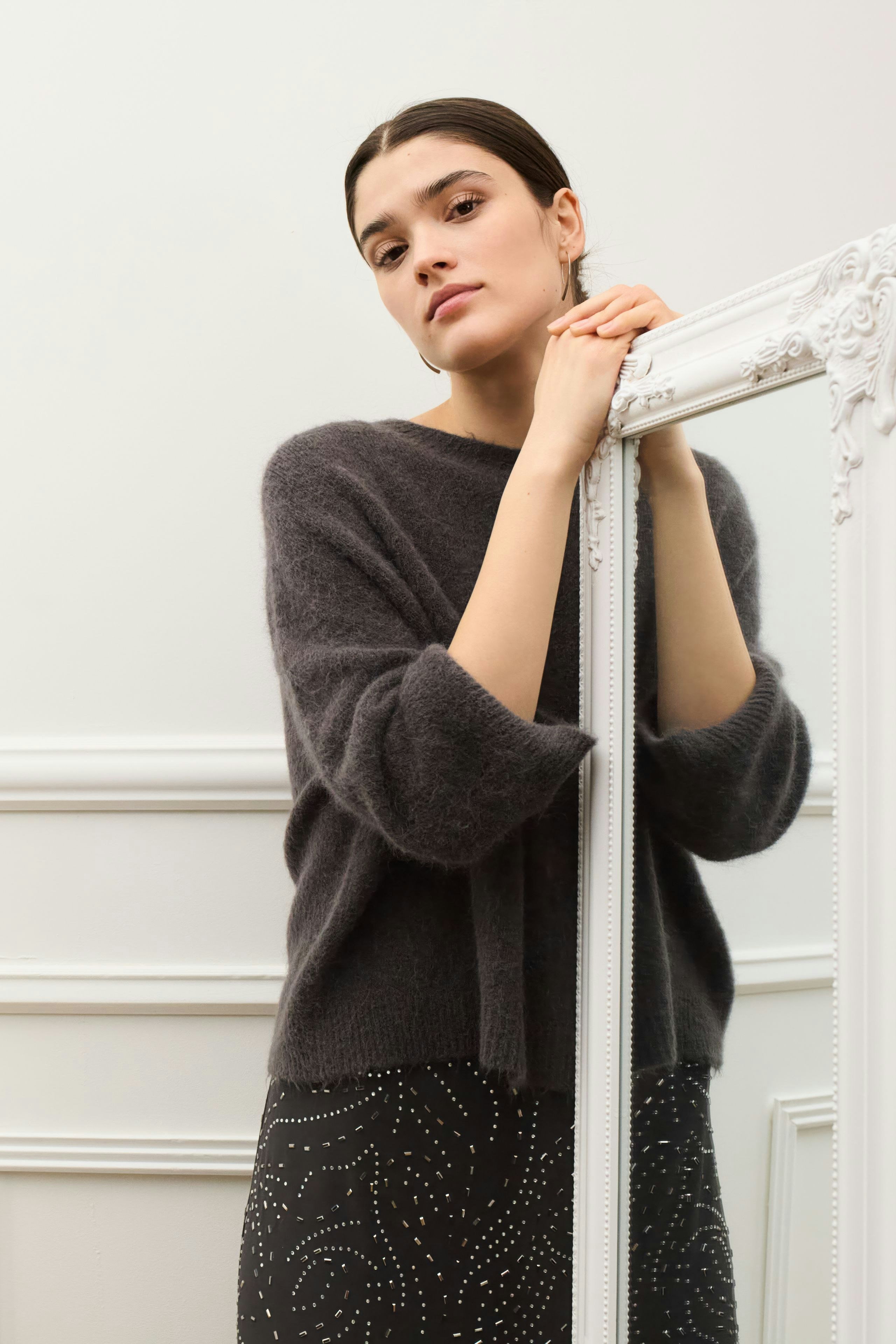 Casual women's pullover: A woman in a cozy gray pullover poses confidently beside a mirror.