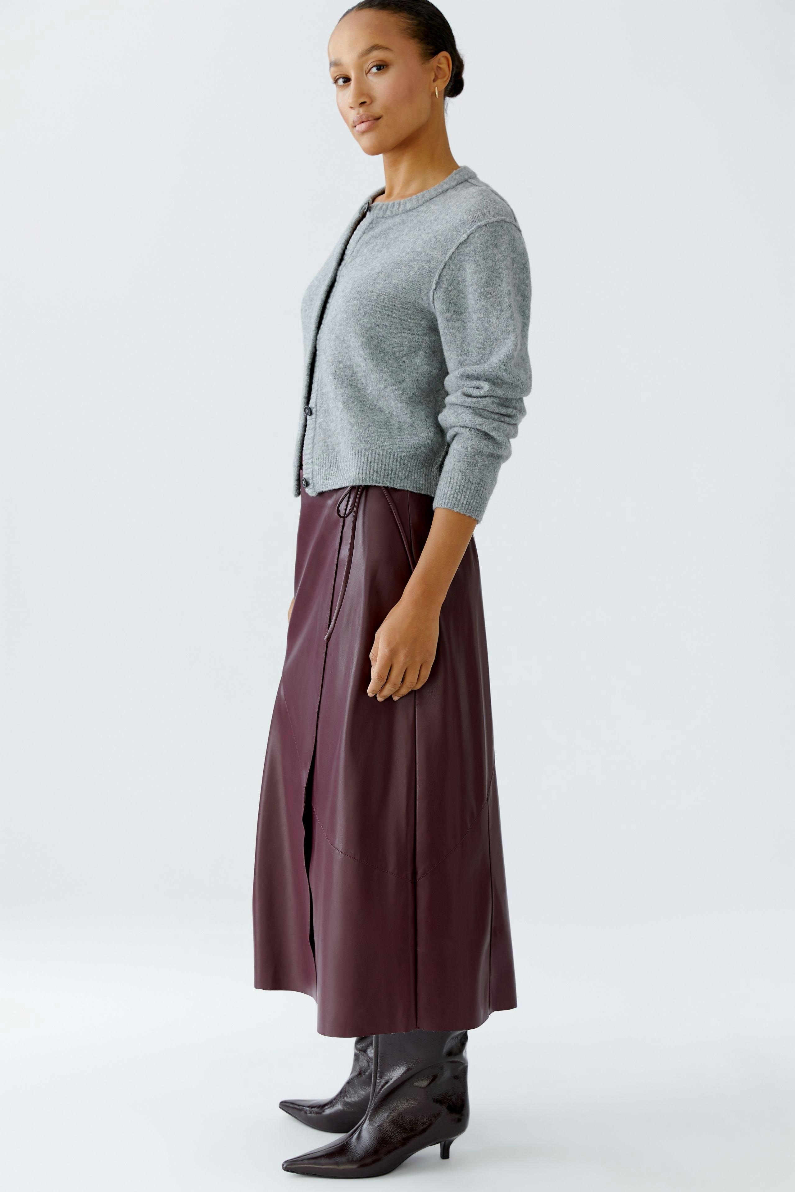 Modern wrap skirt: Woman in a burgundy wrap skirt paired with a grey pullover and stylish boots.