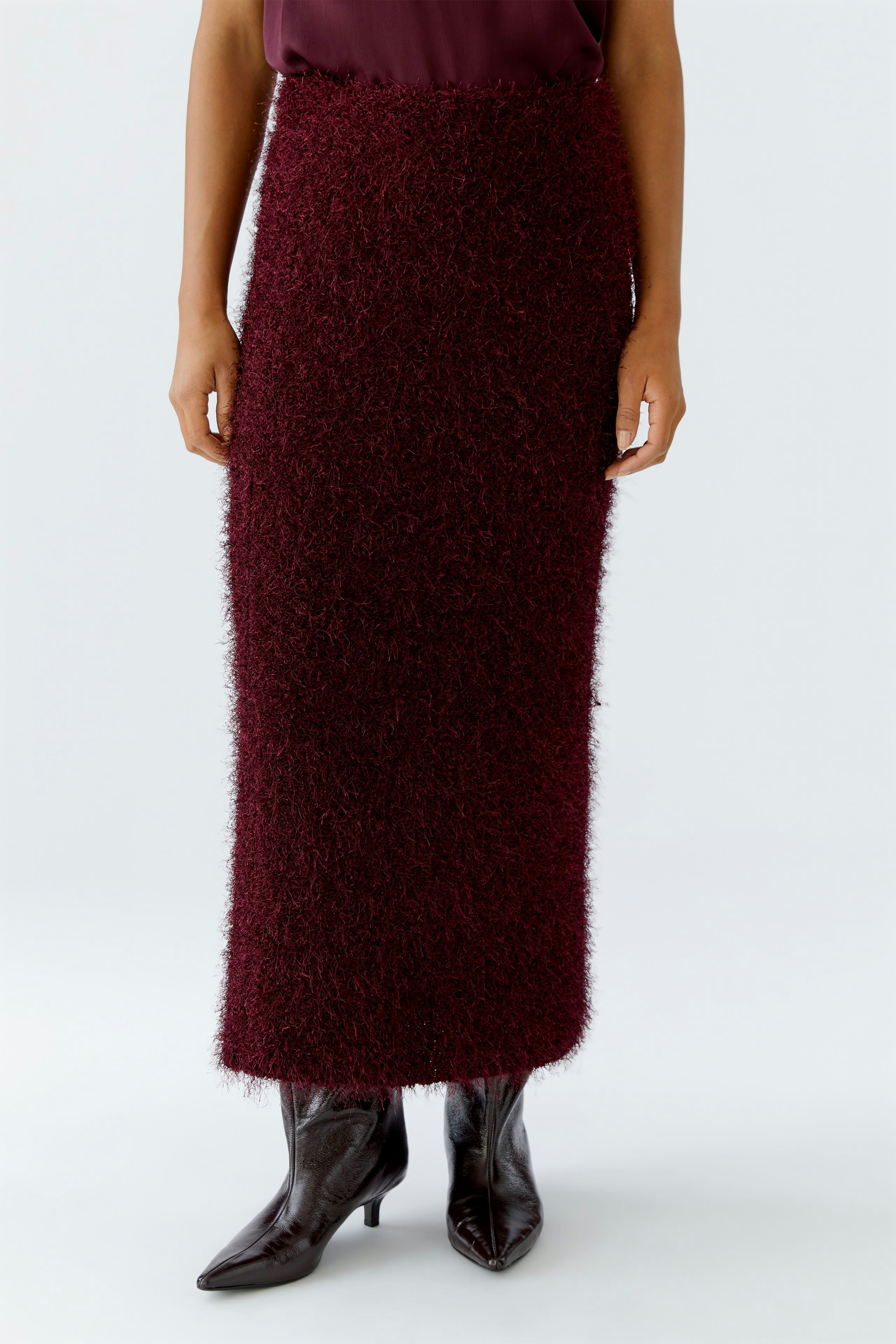 Damen-Strickrock: Frau trägt einen burgunderfarbenen, flauschigen Strickrock, kombiniert mit hohen Stiefeln.