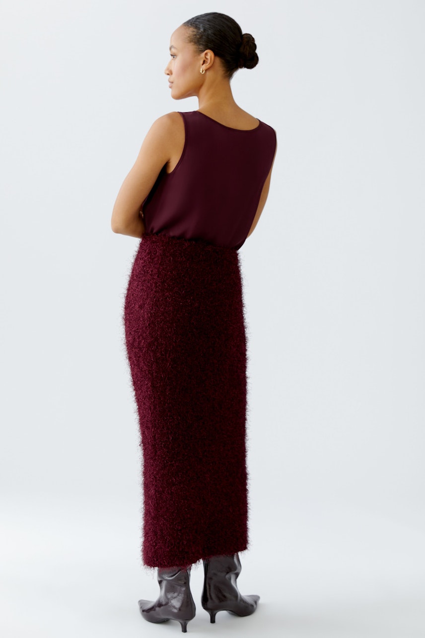 Modern women's knitted skirt: A woman in a burgundy fluffy skirt and top stands confidently.