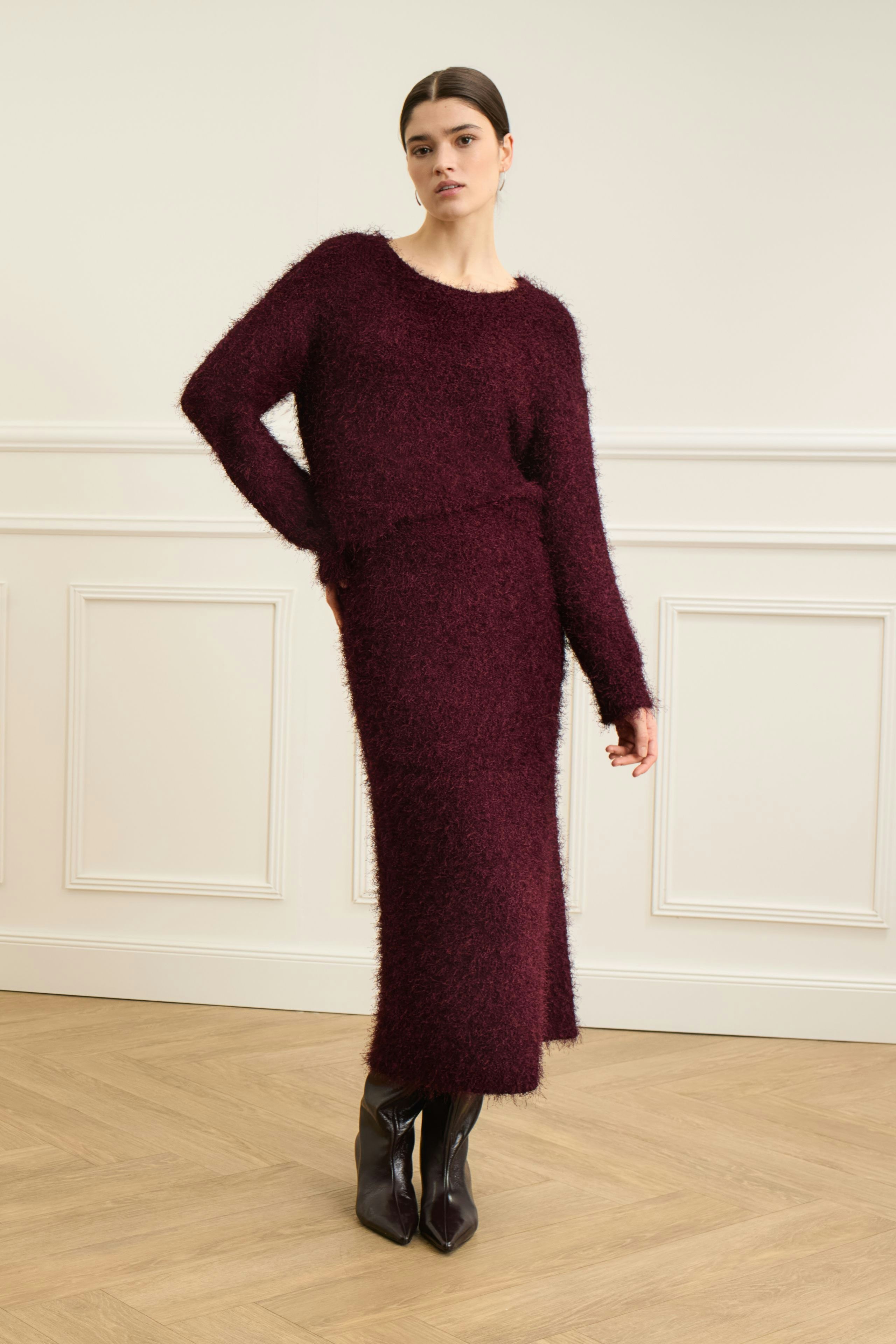 Damen-Strickrock: Frau in burgunderfarbenem Strickrock und passendem Pullover steht selbstbewusst.