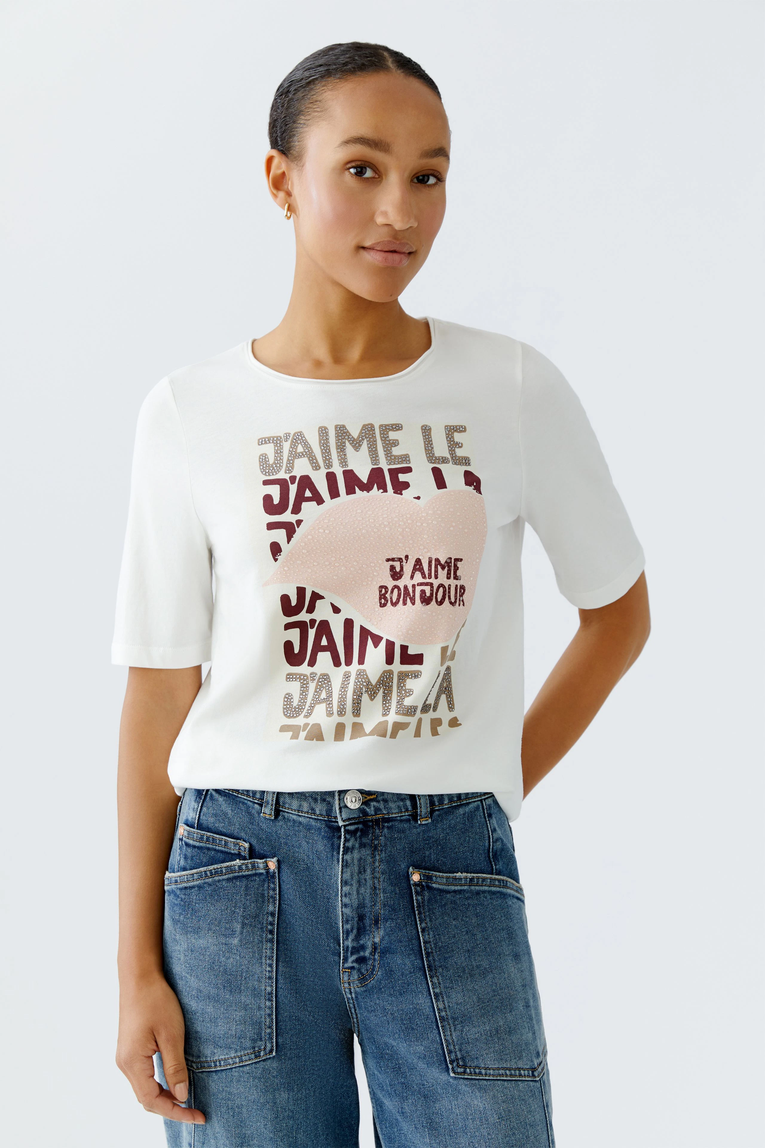 Damen-T-Shirt: Junge Frau trägt ein weißes T-Shirt mit buntem Schriftzug und lässigen Jeans.